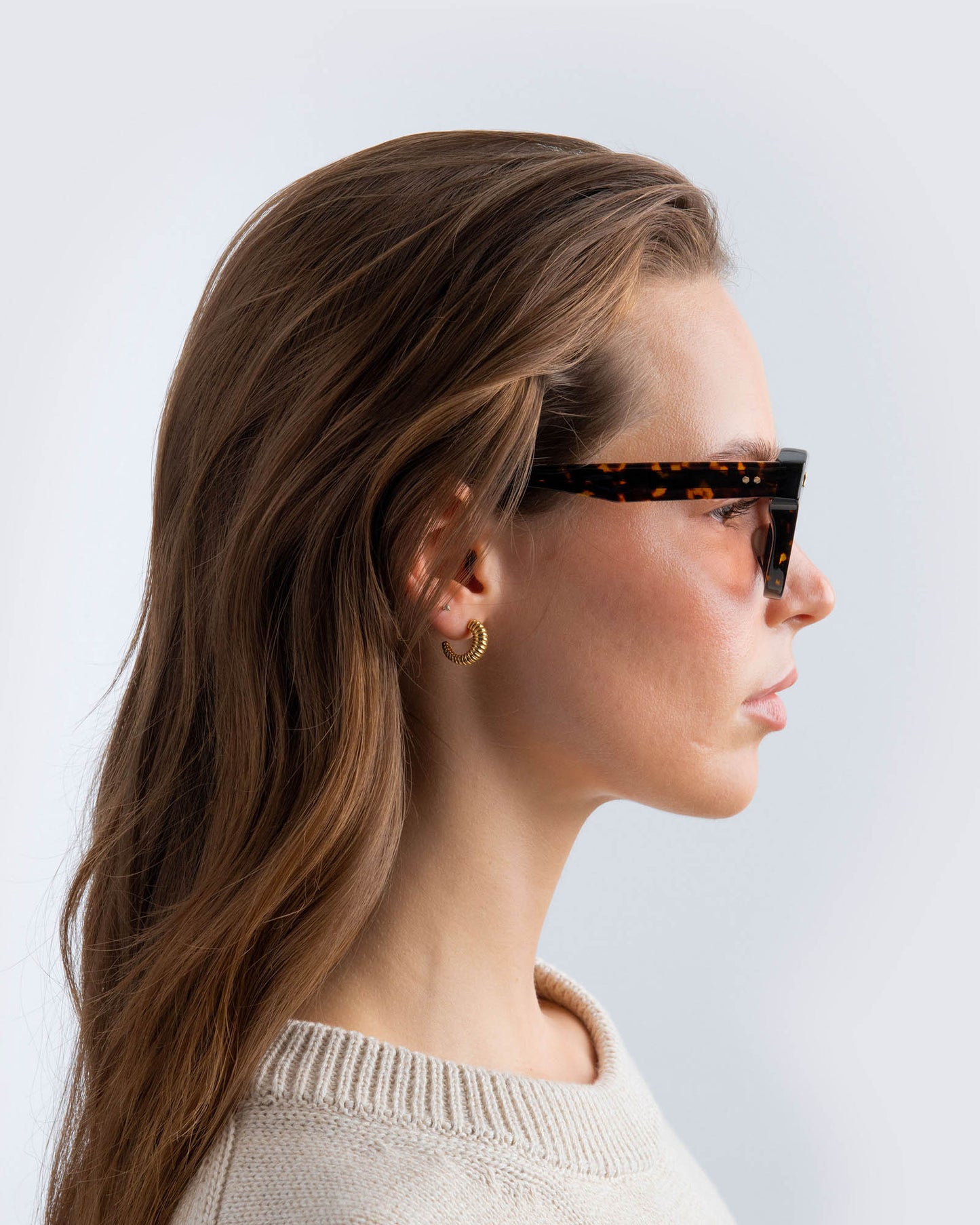 Woman wearing tortoiseshell cat-eye sunglasses with brown lenses against a light gray background