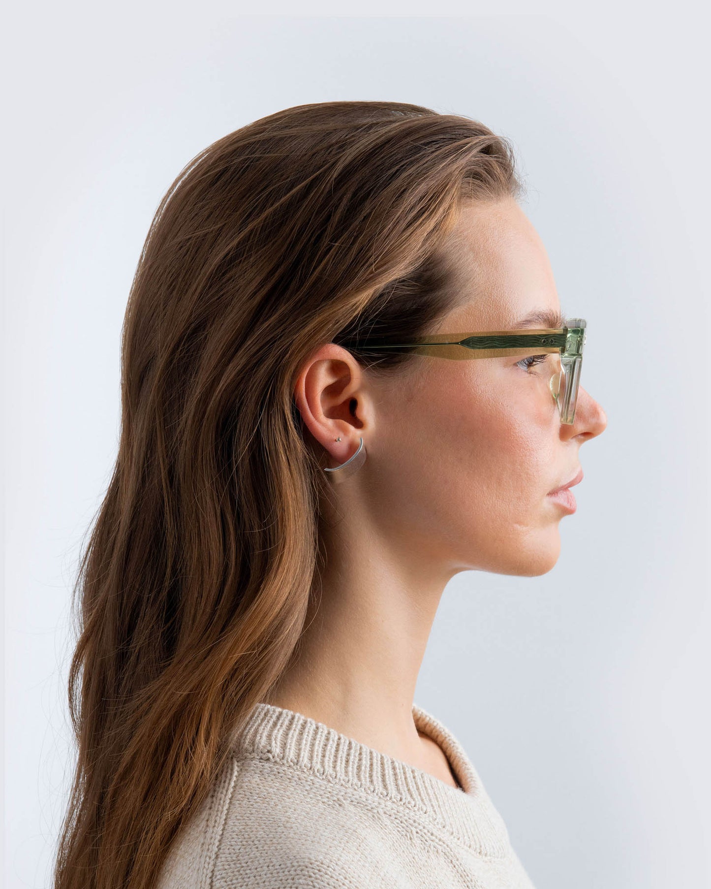 Woman wearing seafoam green sunglasses with lilac lenses against a light grey background