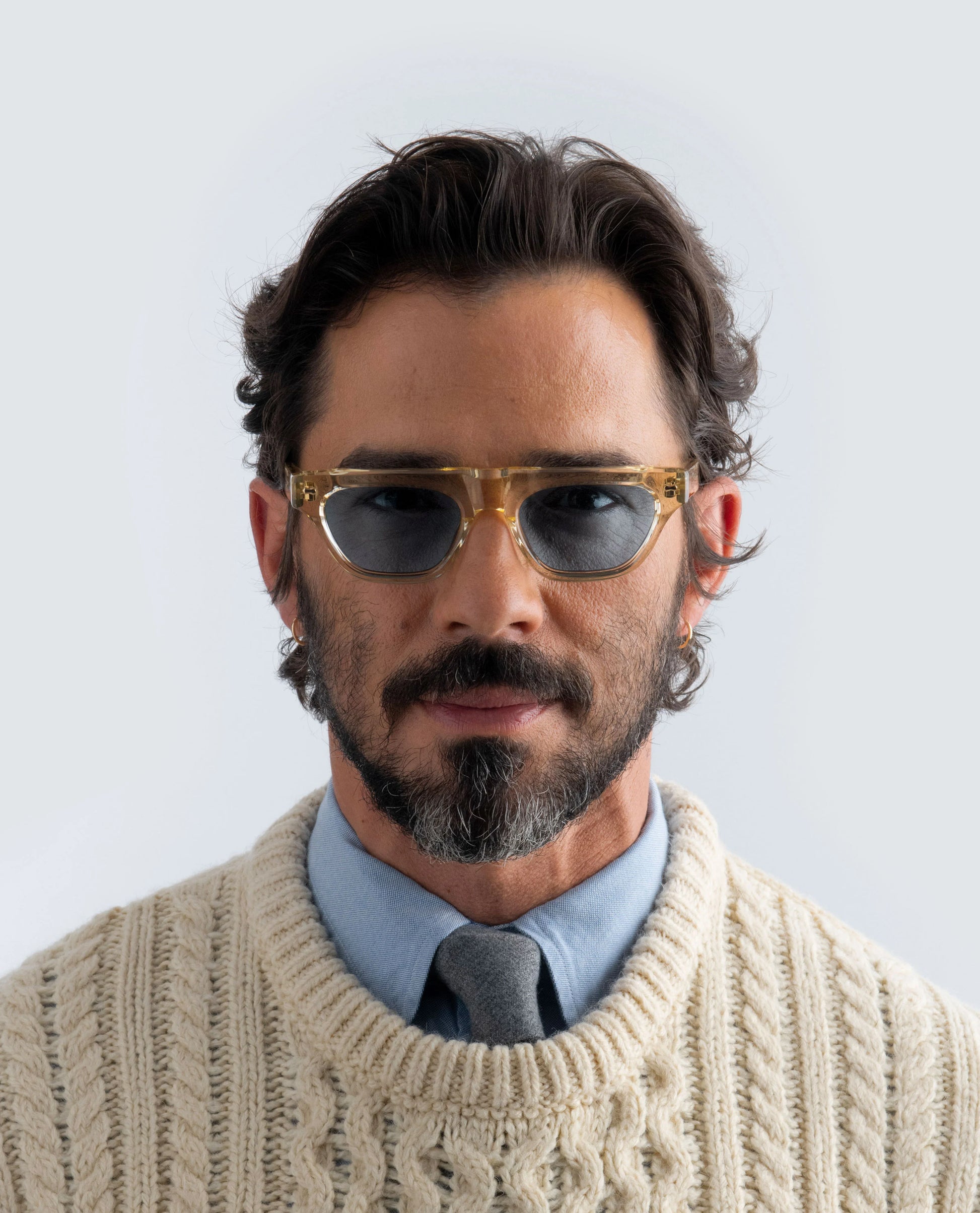Man wearing yellow sunglasses with blue lens and a beige sweater on a light background