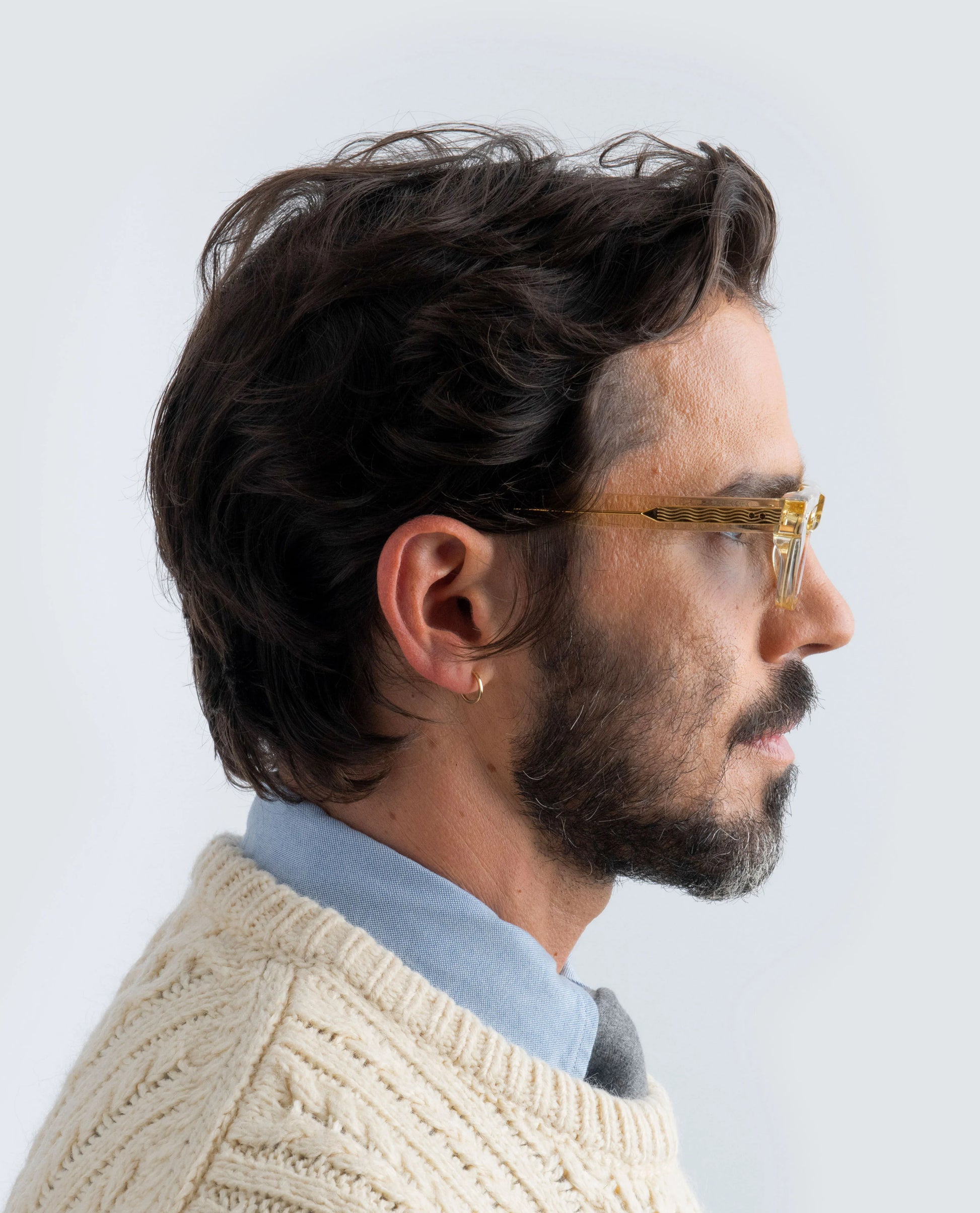 Man wearing yellow sunglasses with blue lens and a beige sweater on a light background