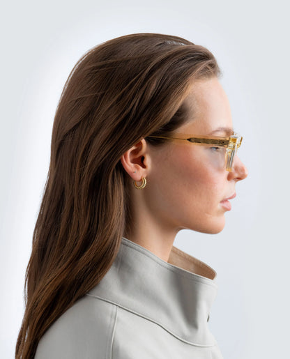 Woman wearing yellow sunglasses with blue lens and a beige coat on a light background