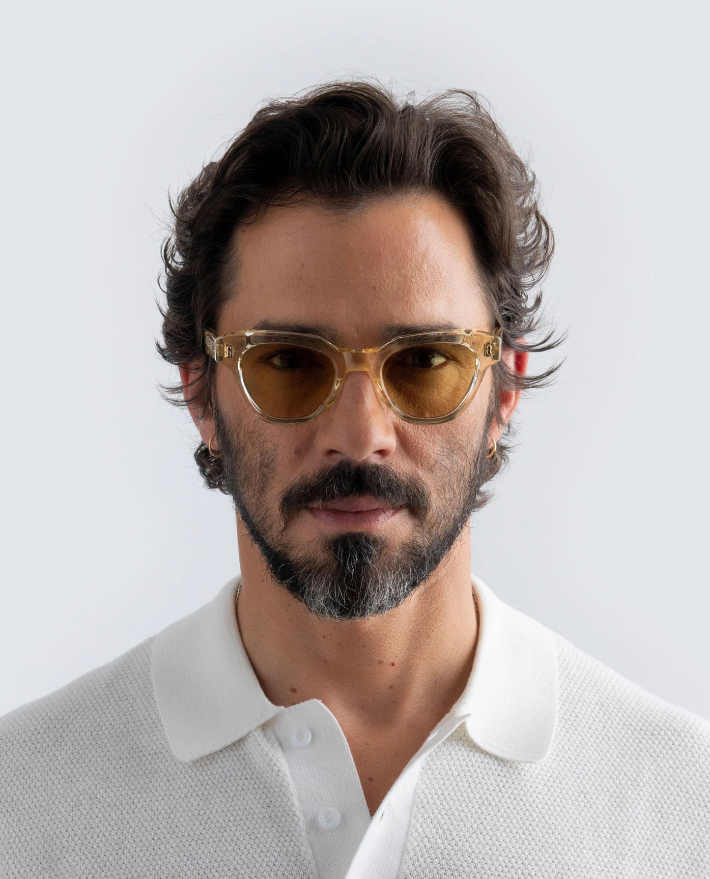 Man wearing Yellow sunglasses with yellow lens and a white shirt against a light background