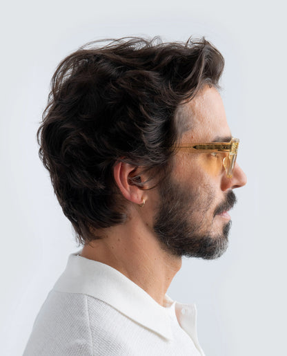 Man wearing Yellow sunglasses with yellow lens and a white shirt against a light background