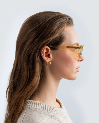 Woman wearing yellow sunglasses with yellow lens and a beige sweater against a light background
