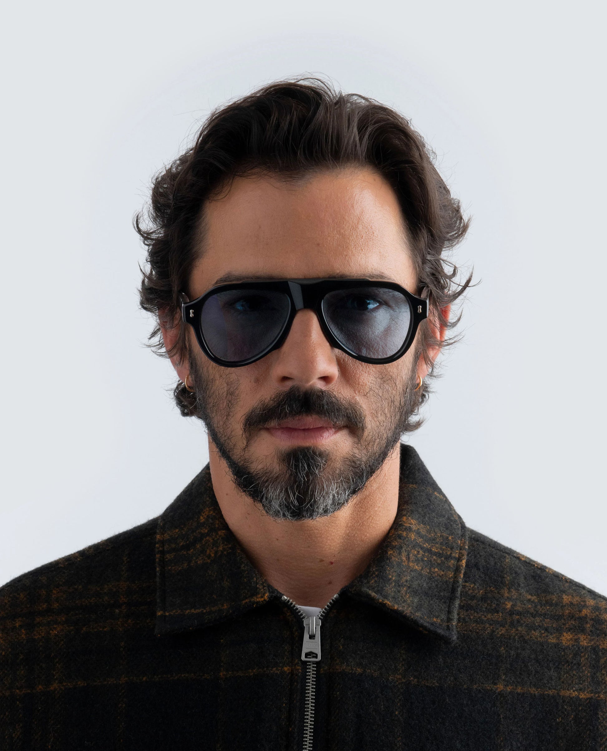 Man wearing black sunglasses and a dark jacket against a light background