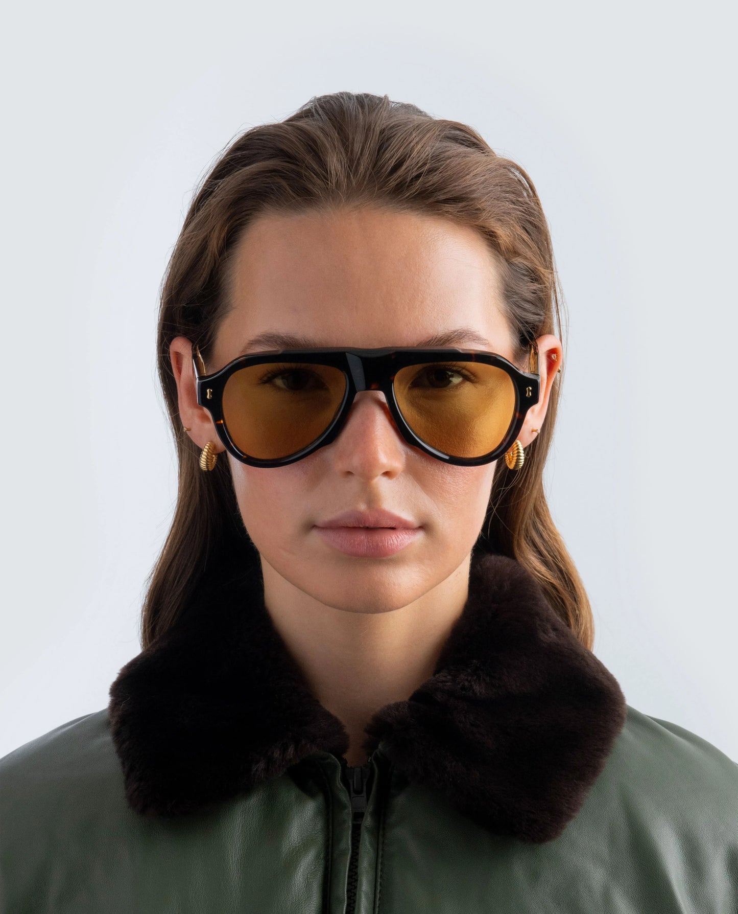 Woman wearing Havana sunglasses with amber lens and a dark jacket against a light background