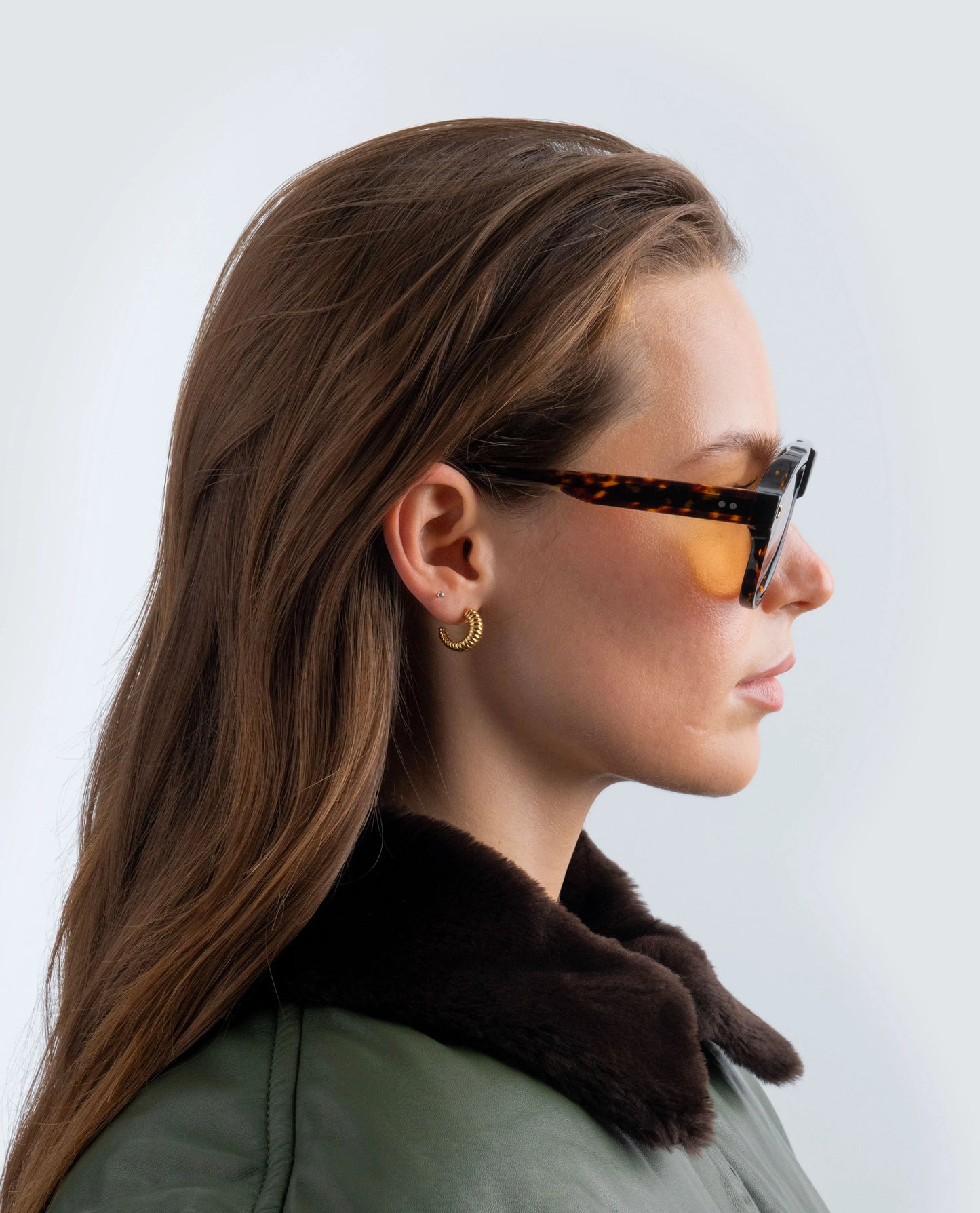 Woman wearing Havana sunglasses with amber lens and a dark jacket against a light background