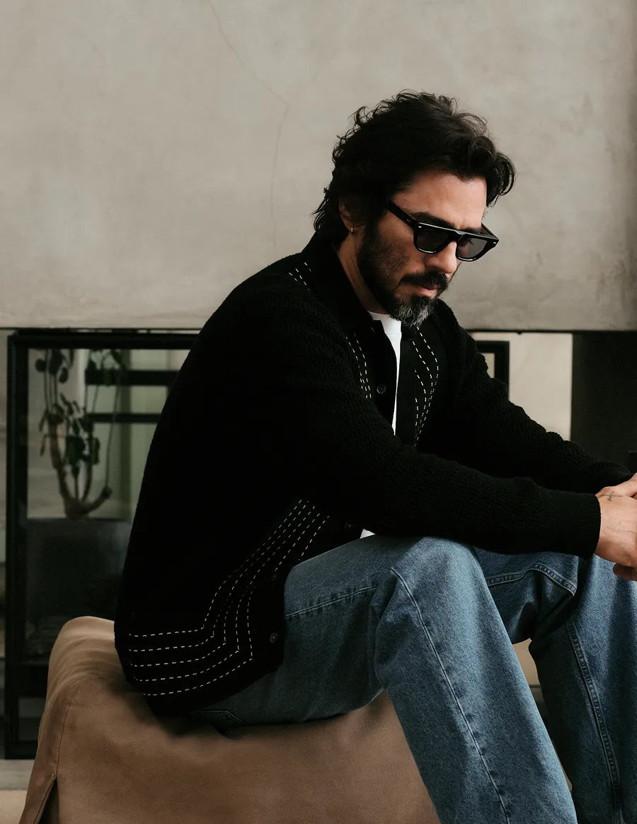 Man sitting on a couch wearing black sunglasses with black lenses in a modern living room