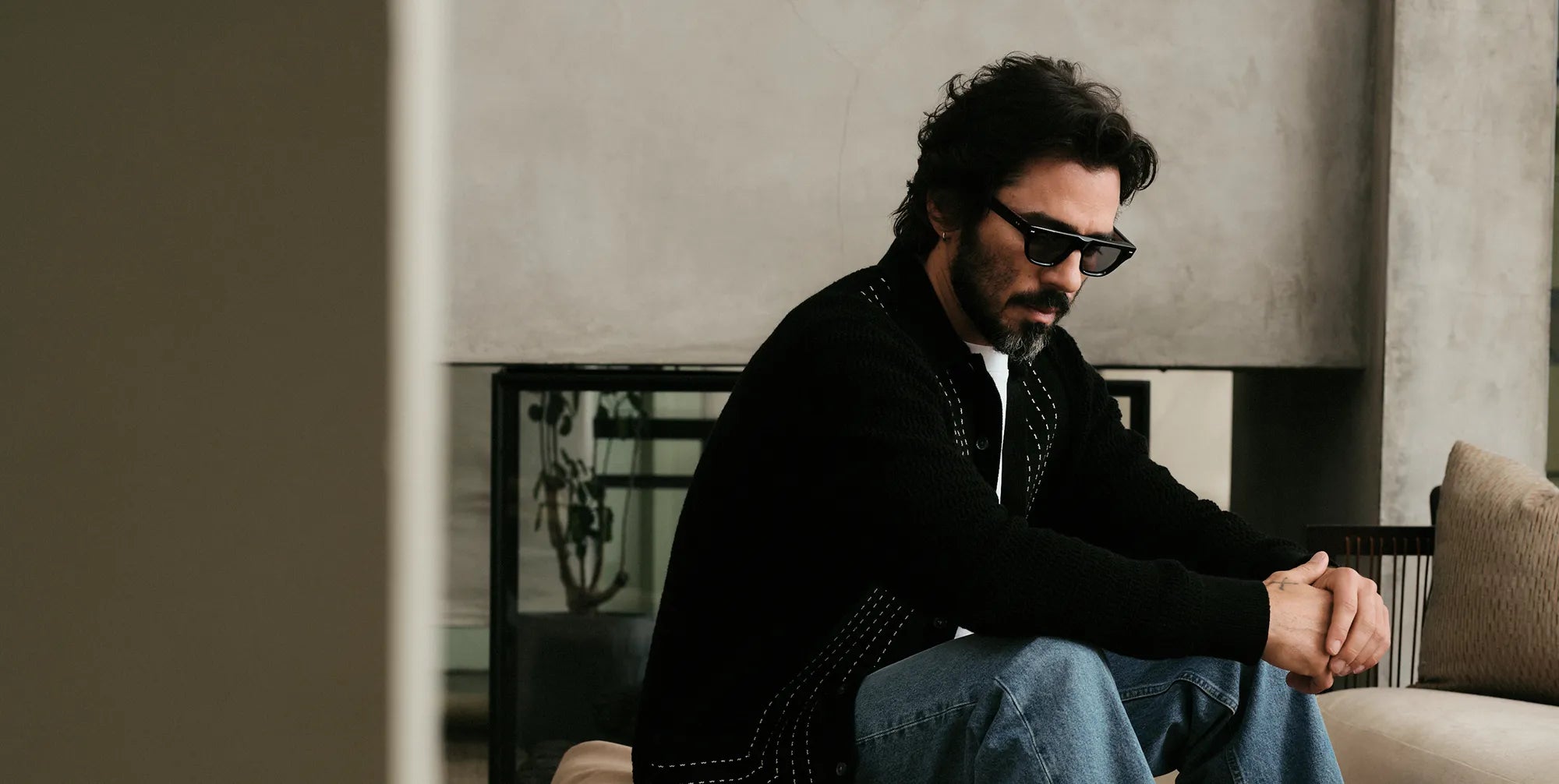 Man sitting on a couch wearing black sunglasses with black lenses in a modern living room
