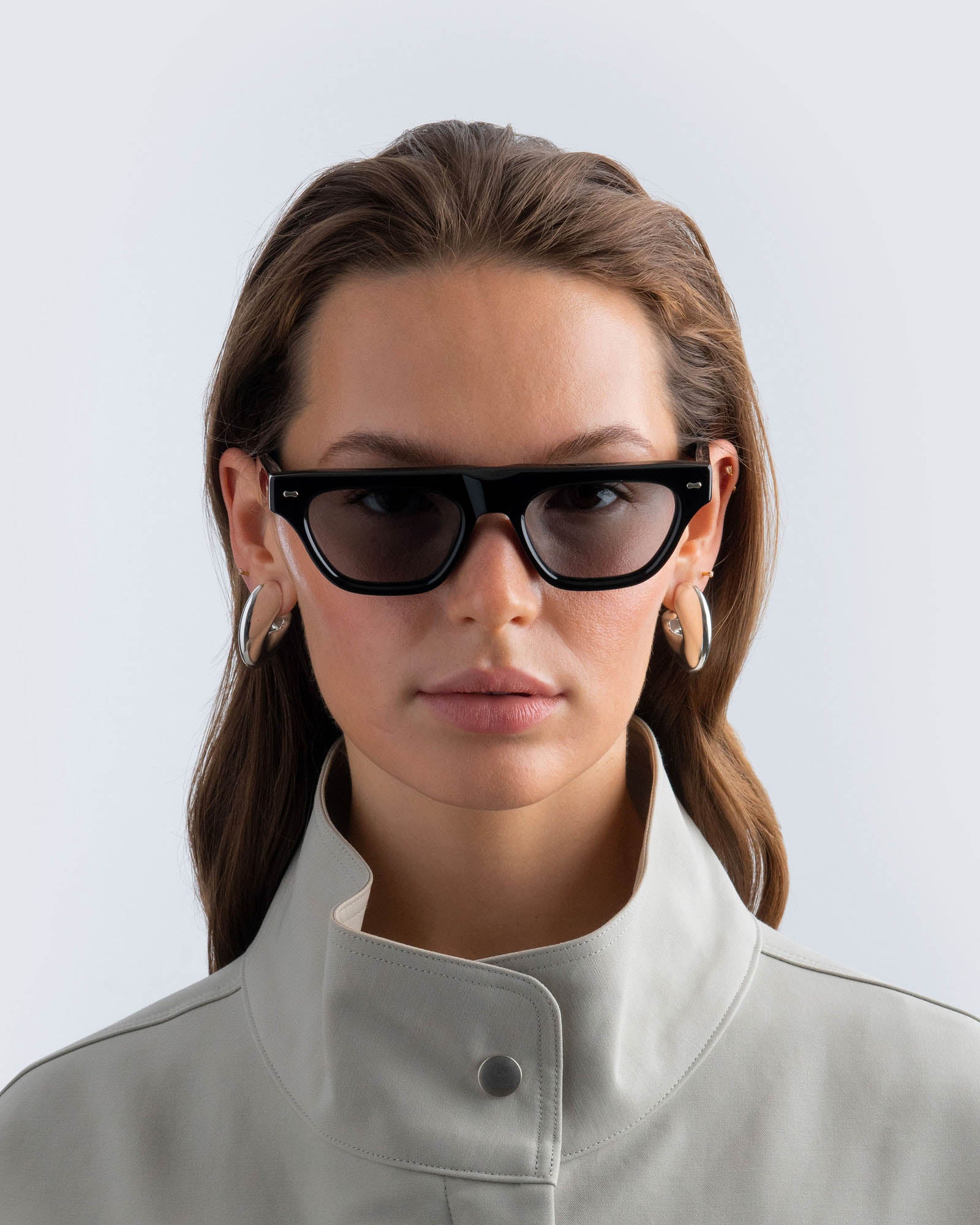 Woman wearing black sunglasses with grey lenses against a light background