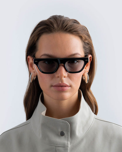 Woman wearing black sunglasses with grey lenses against a light background