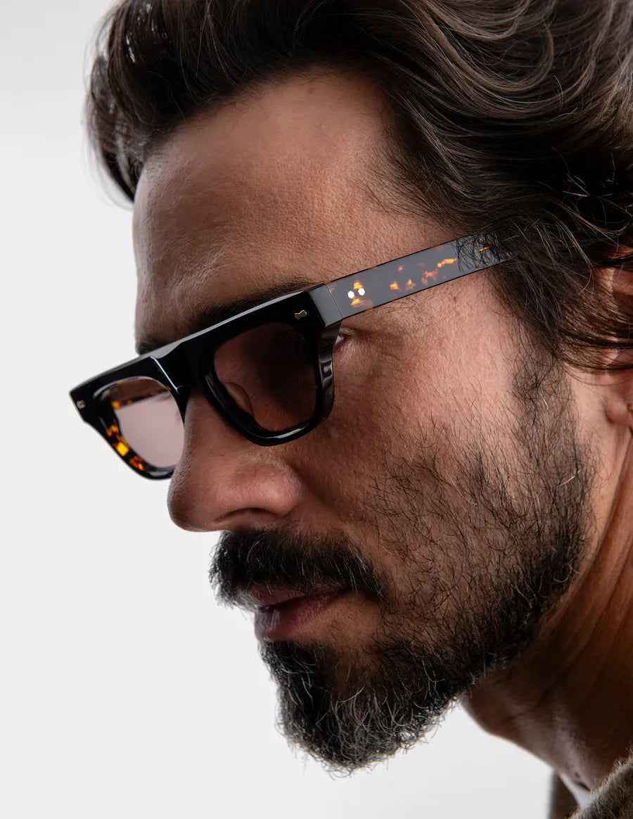 Close-up of a man wearing tortoiseshell sunglasses with brown lenses against a neutral background