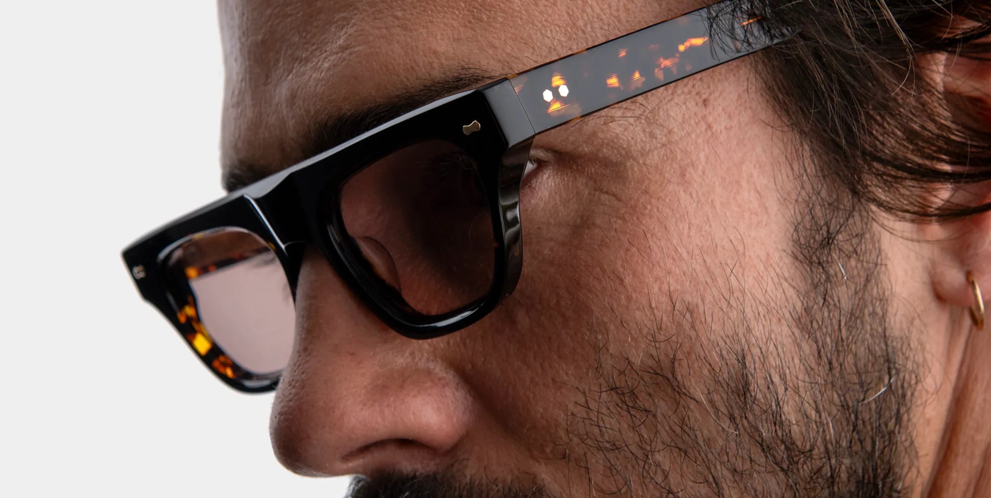 Close-up of a man wearing tortoiseshell sunglasses with brown lenses against a neutral background