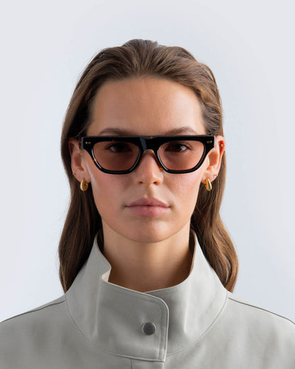 Woman wearing tortoiseshell sunglasses with brown lenses against a light background
