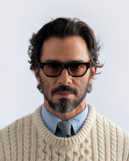 Man wearing tortoiseshell sunglasses with brown lenses against a light background