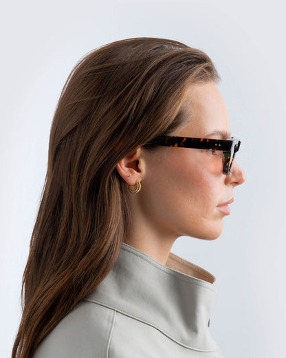 Woman wearing tortoiseshell sunglasses with brown lenses against a light background
