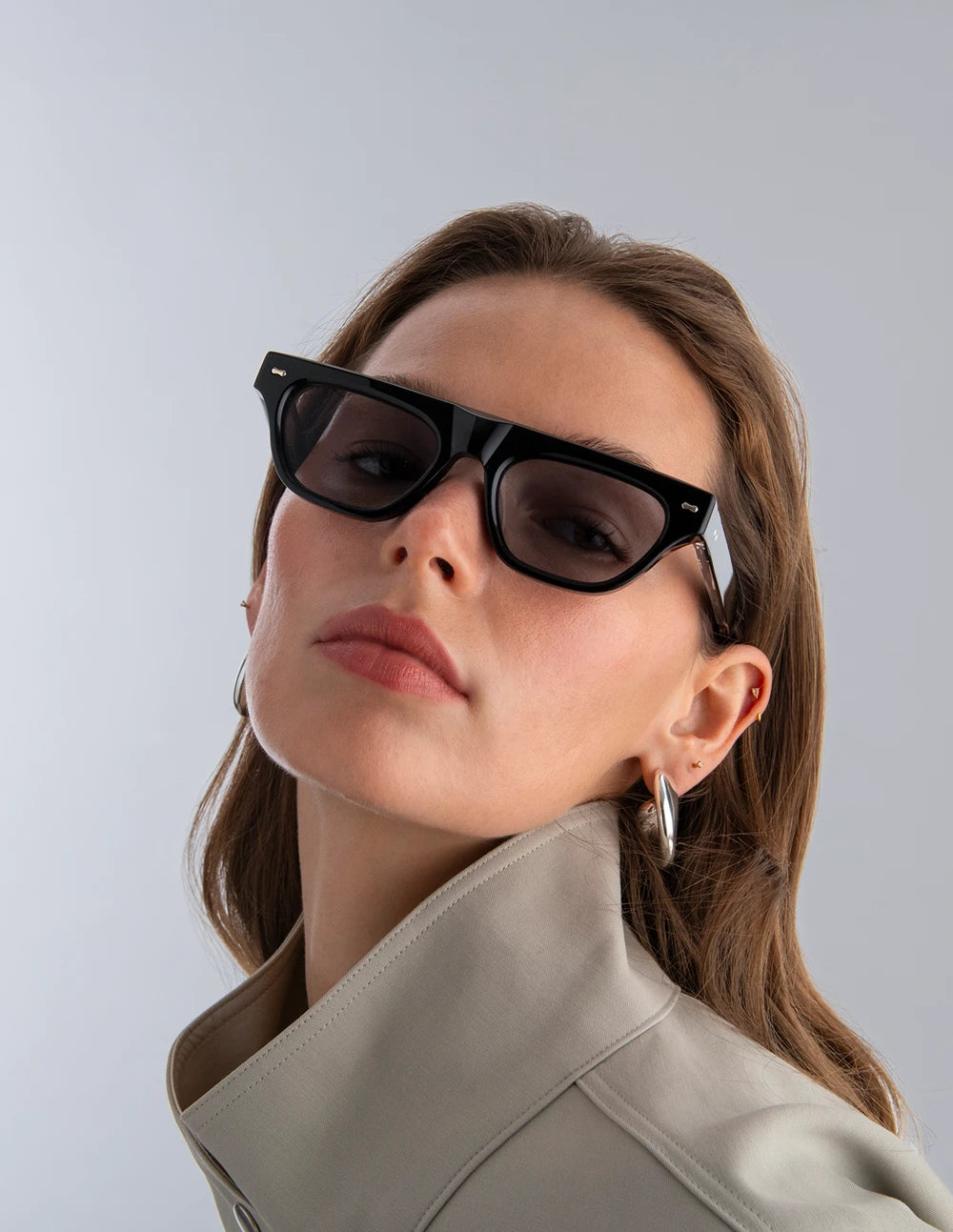Woman wearing black sunglasses with black lenses against a light gray background