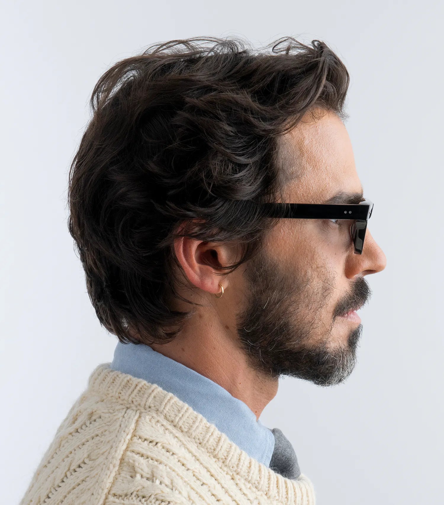 Man wearing black sunglasses with black lenses and a beige sweater with a light background