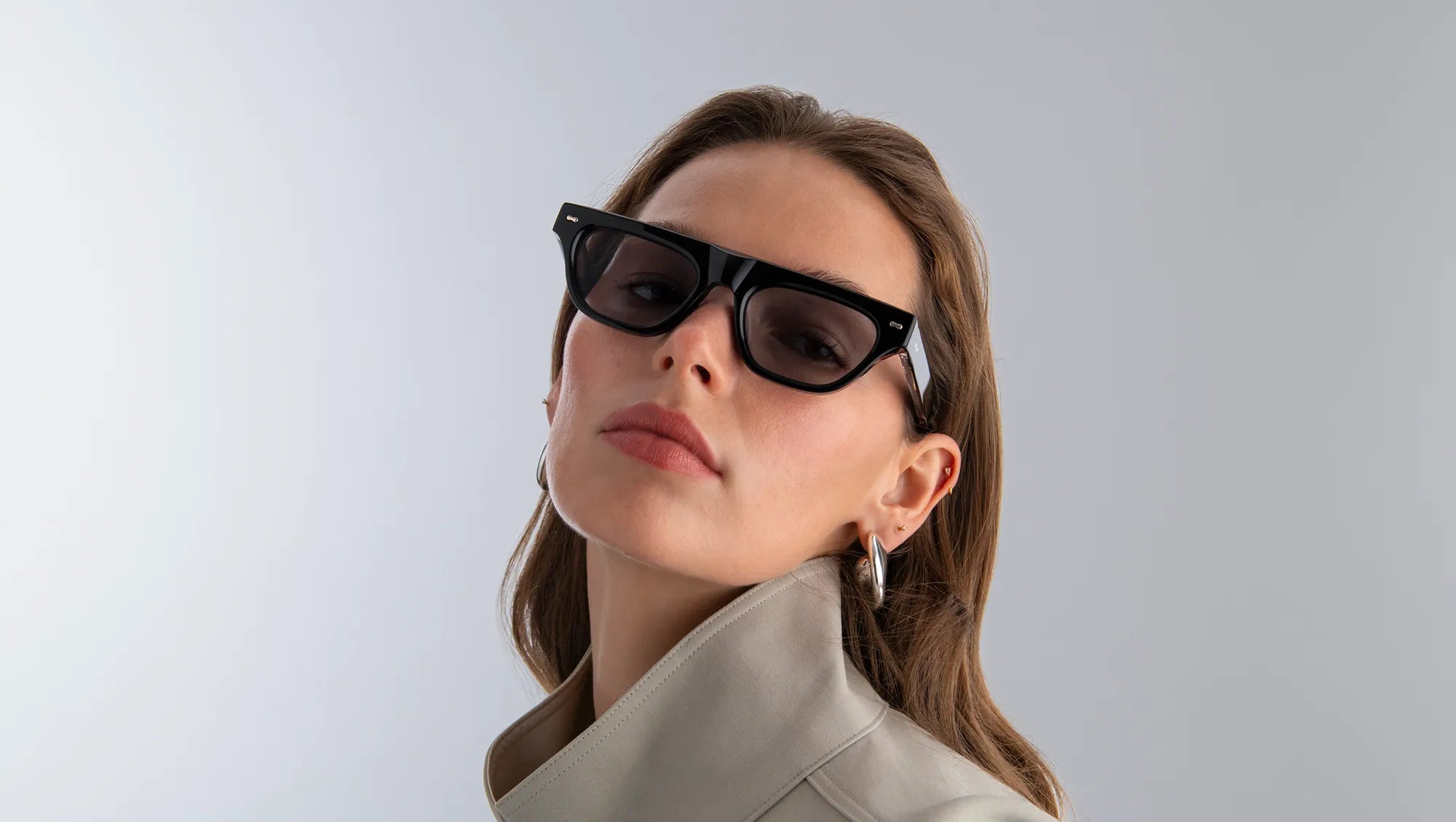 Woman wearing black sunglasses with black lenses against a light gray background