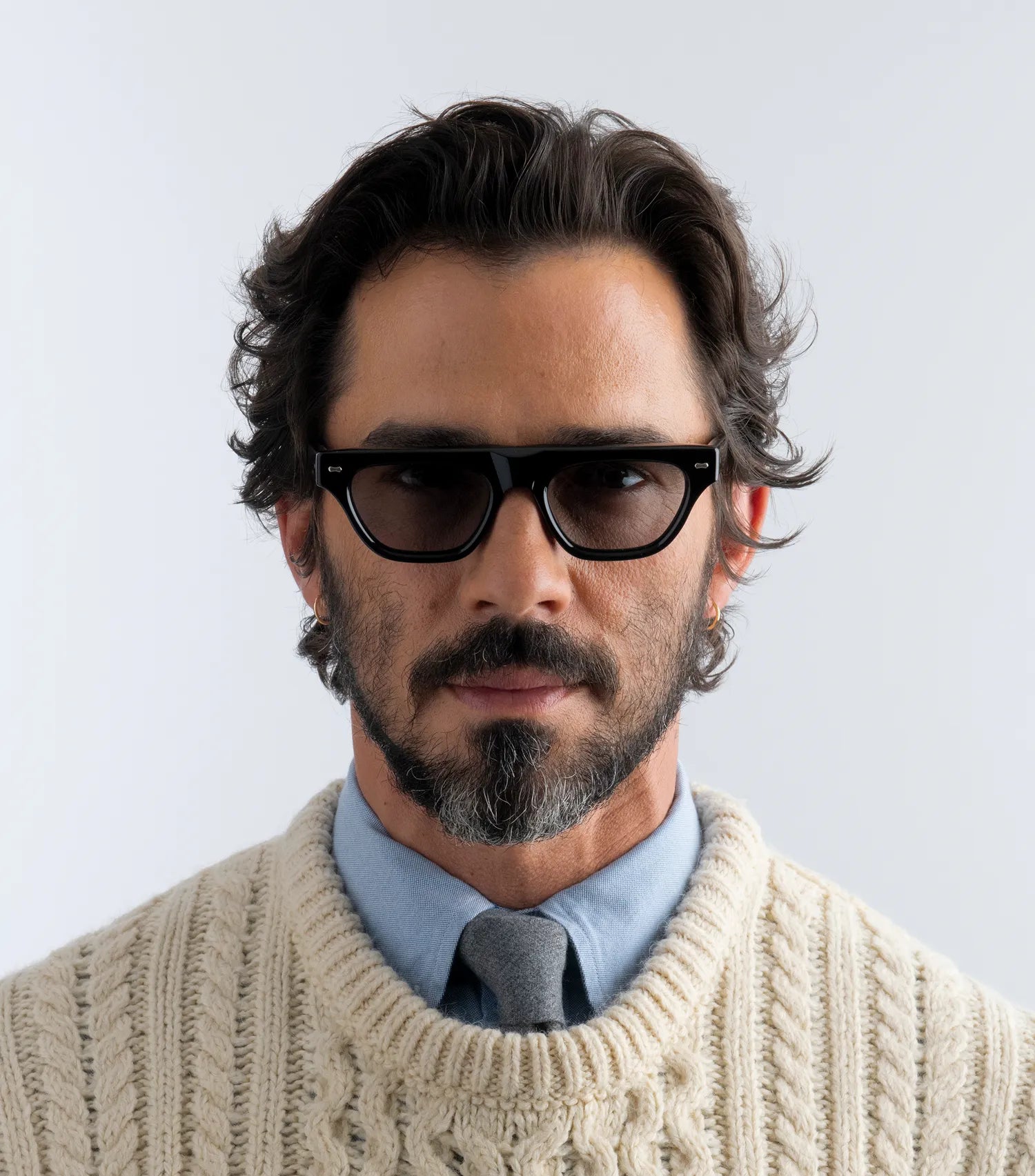 Man wearing black sunglasses with black lenses and a beige sweater with a light background