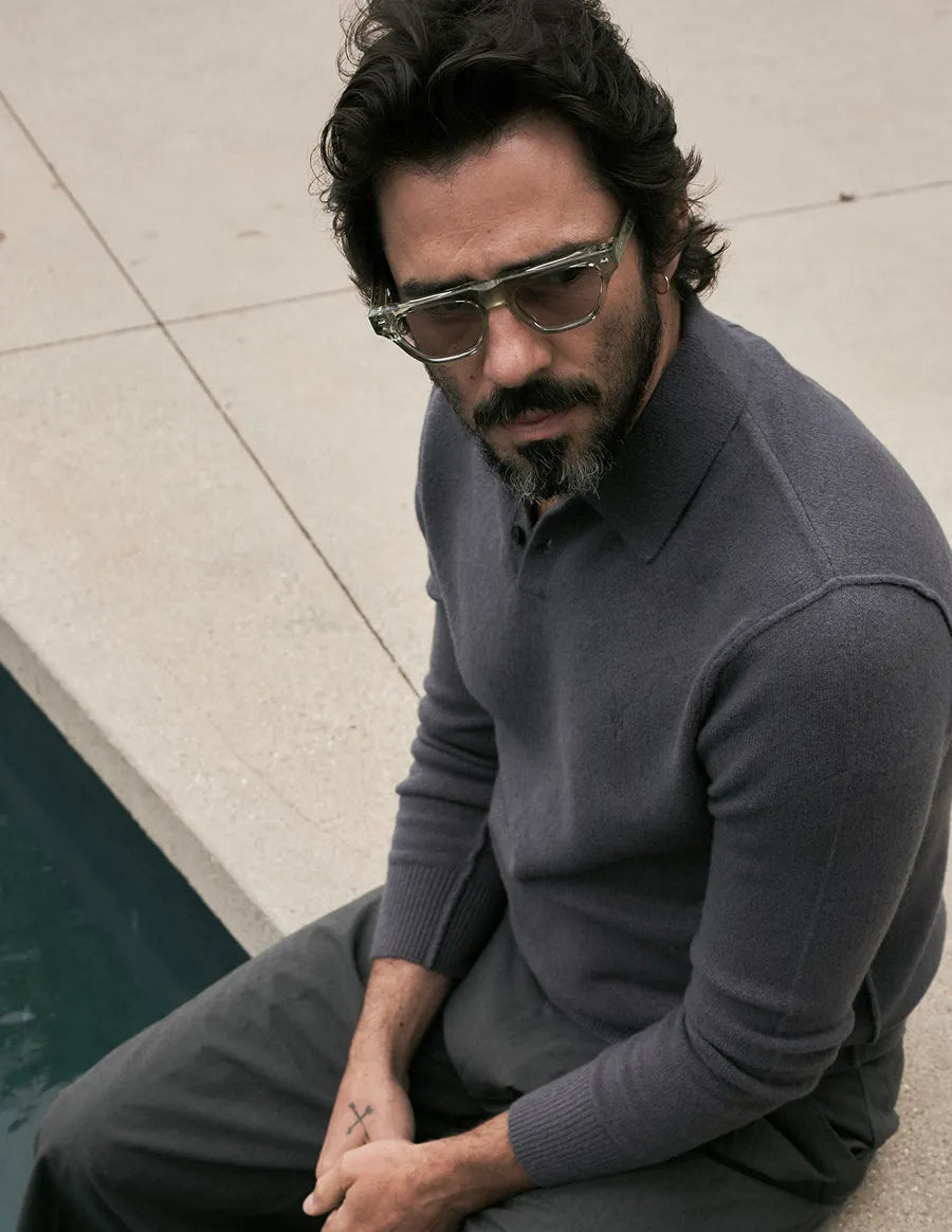 Man wearing seafoam green sunglasses and a gray sweater on a light-colored pavement