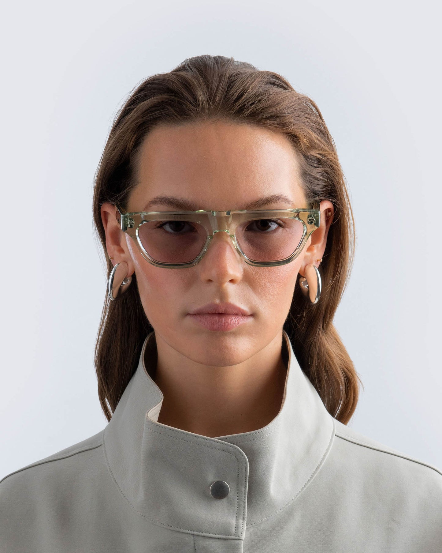 Woman wearing seafoam green sunglasses with lilac lenses against a light background