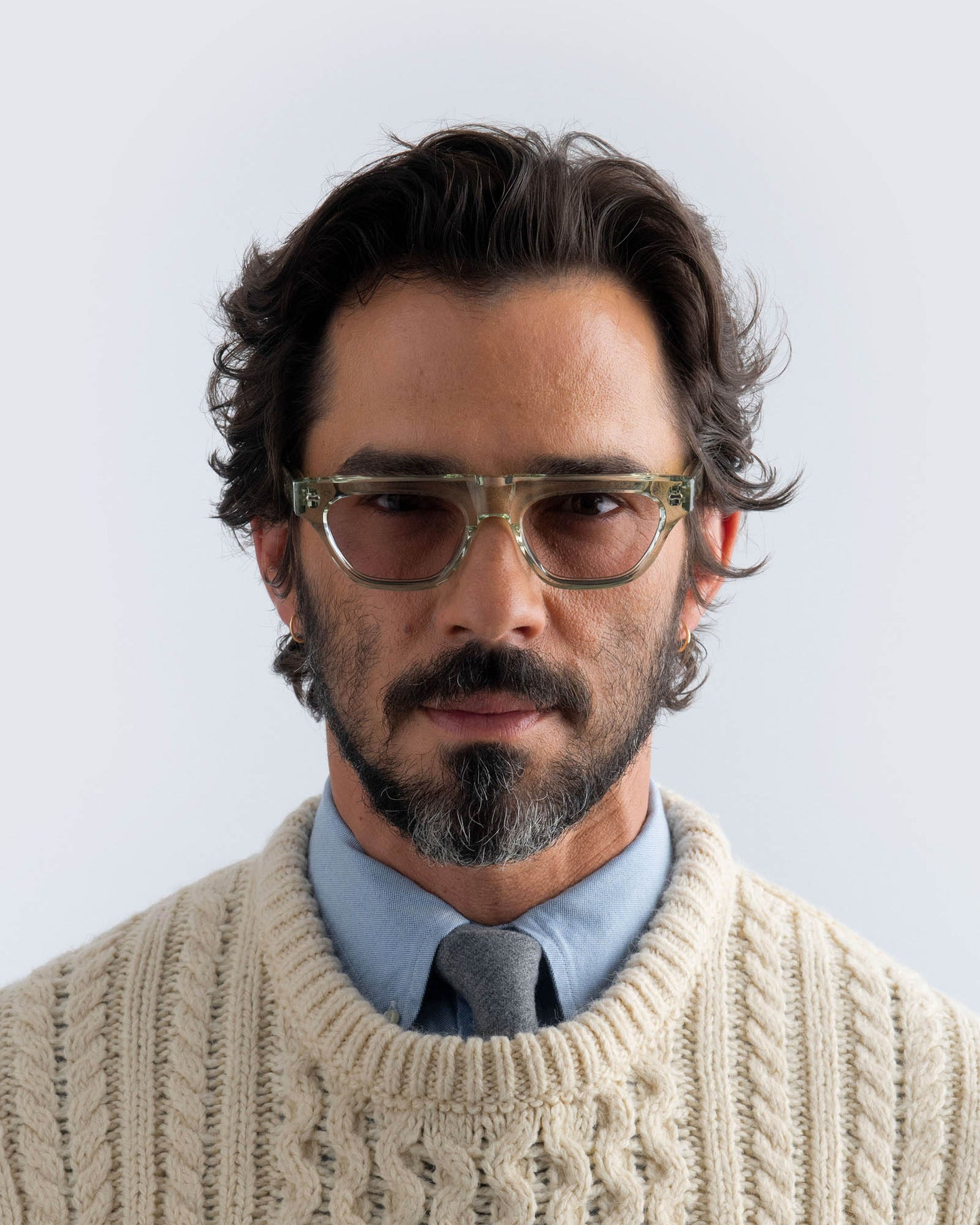 Man wearing seafoam green sunglasses with lilac lenses against a light background