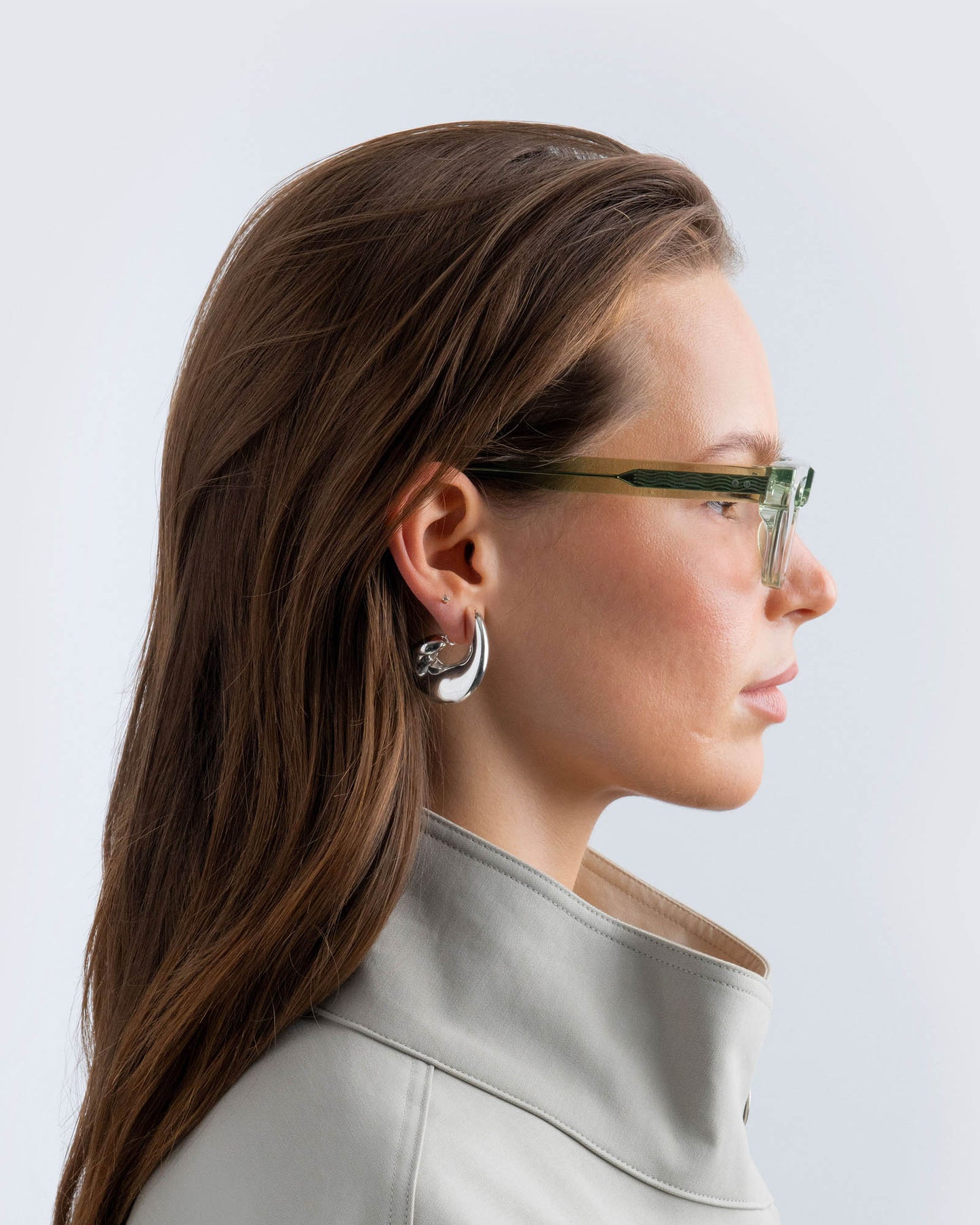Woman wearing seafoam green sunglasses with lilac lenses against a light background