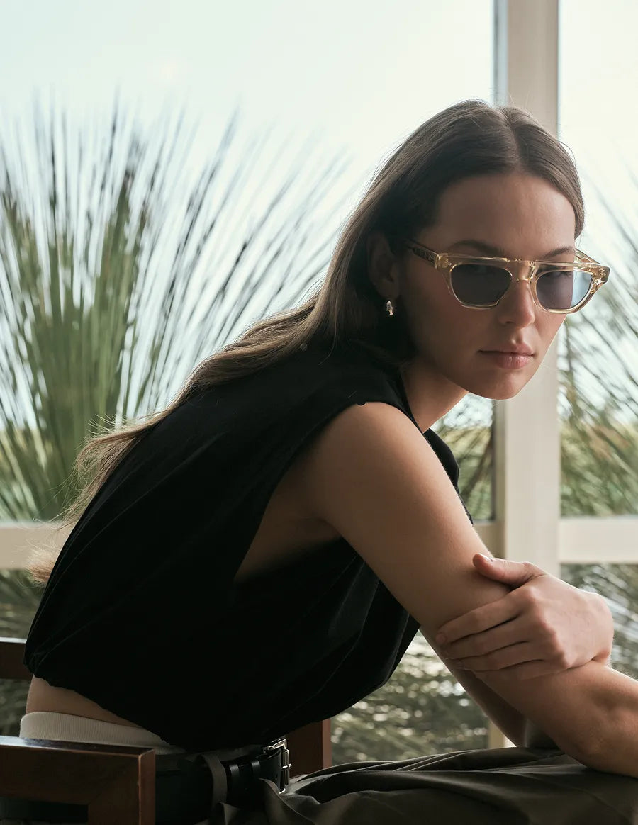 Woman wearing yellow sunglasses with blue lenses with a blurred natural background