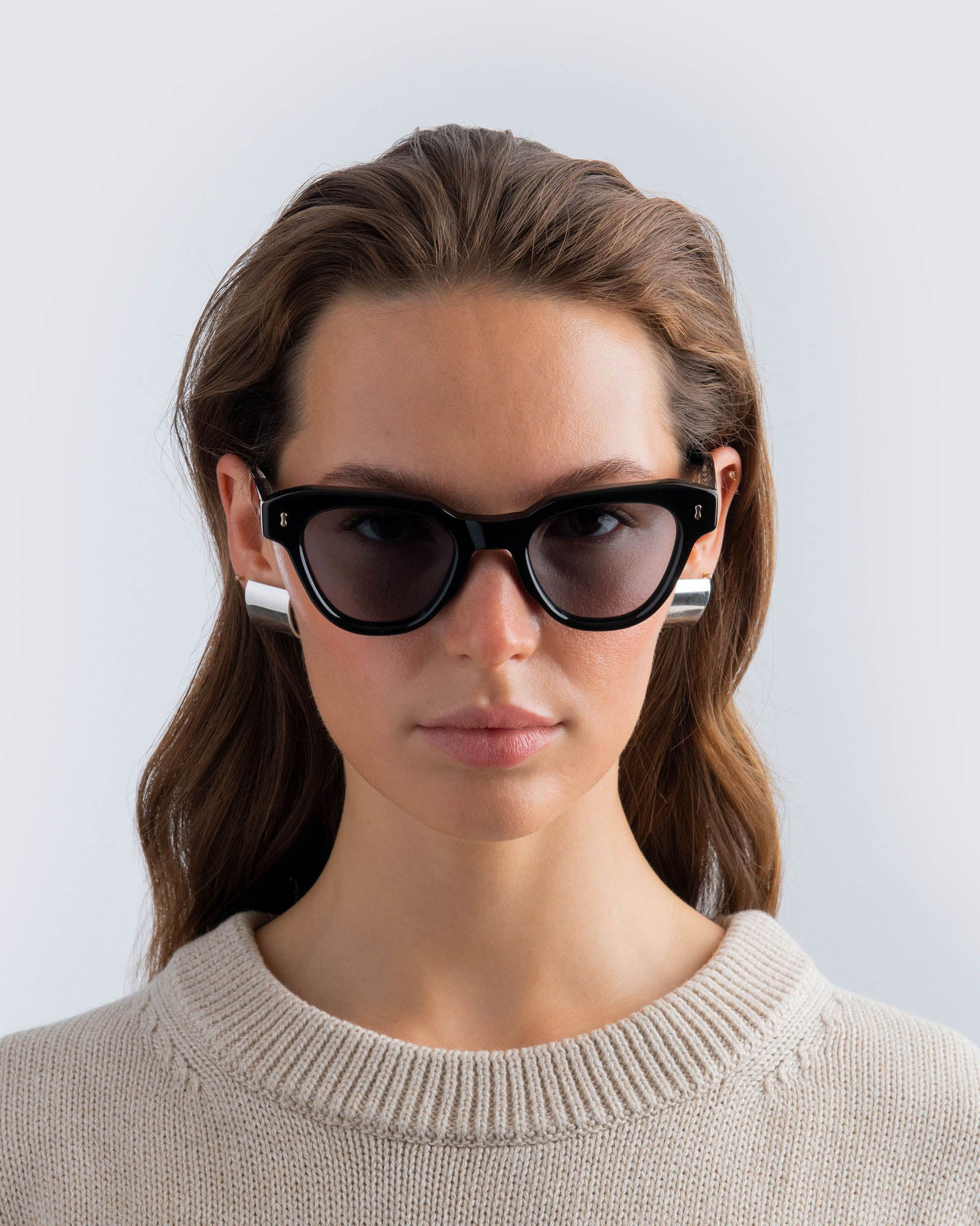 Woman wearing black cat-eye sunglasses with grey lenses against a light gray background