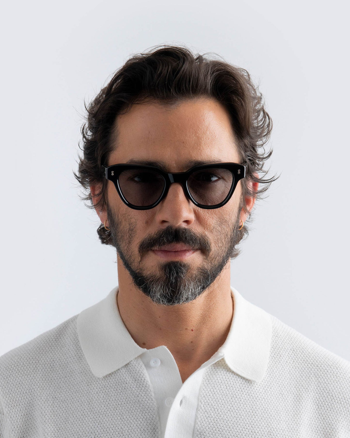 Man wearing black cat-eye sunglasses with grey lenses against a light gray background