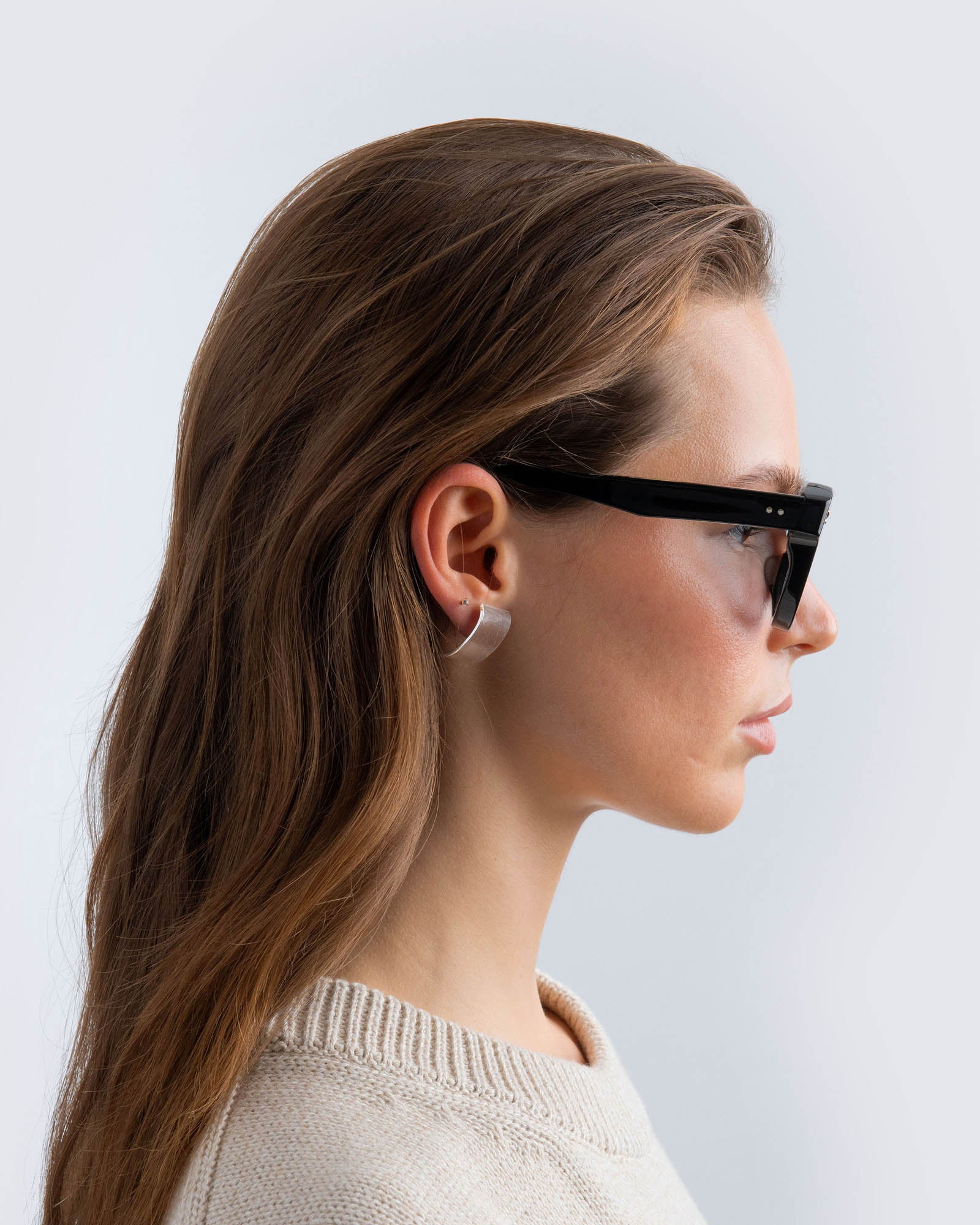 Woman wearing black cat-eye sunglasses with grey lenses against a light gray background