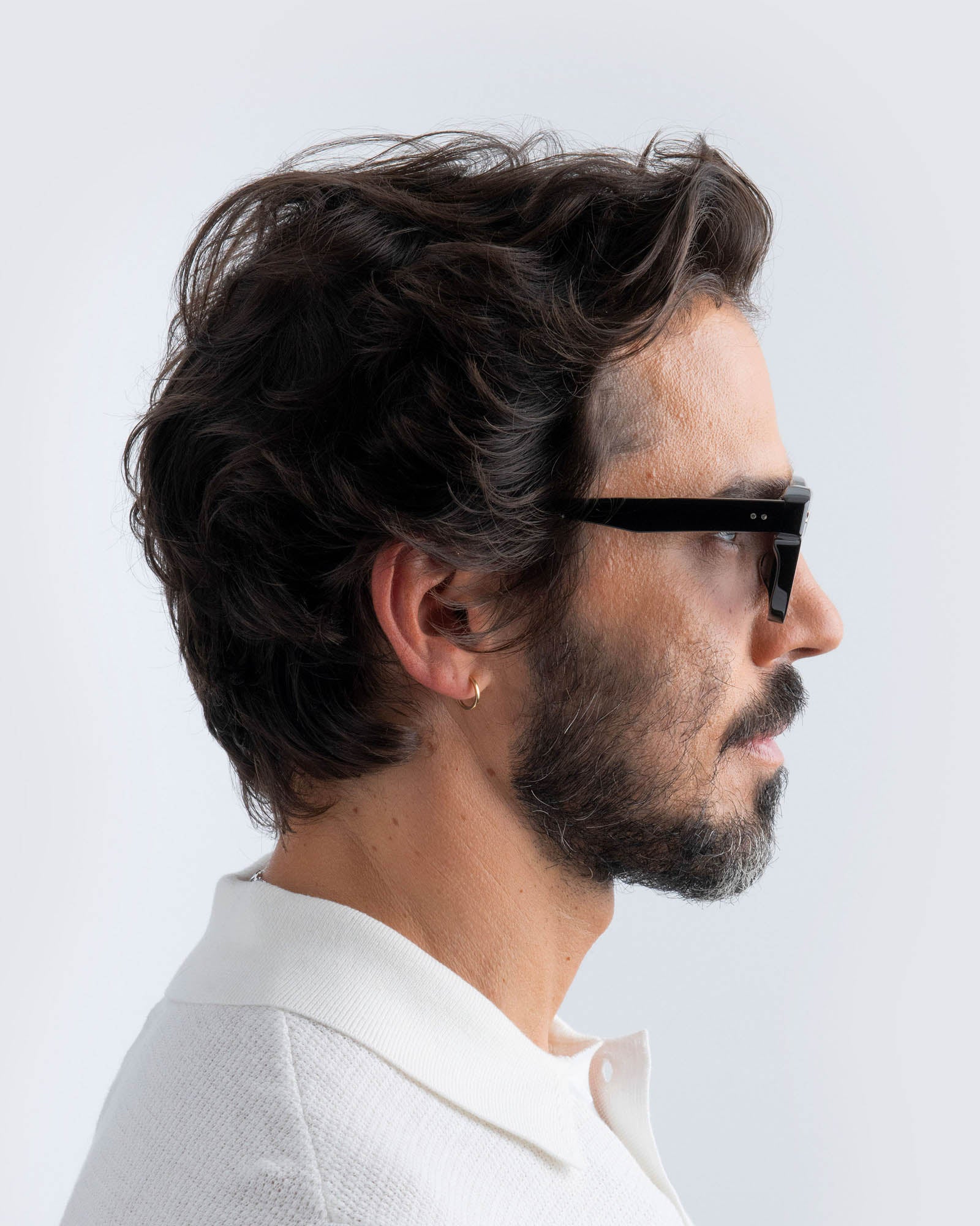 Man wearing black cat-eye sunglasses with grey lenses against a light gray background