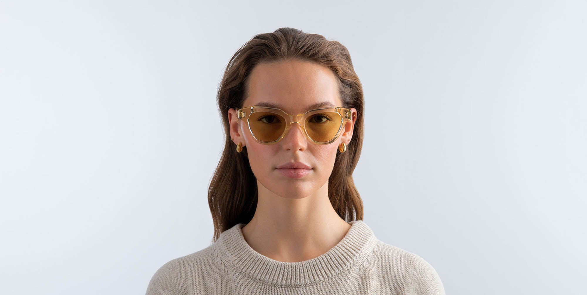 Woman wearing champagne yellow sunglasses with yellow lenses against a light gray background