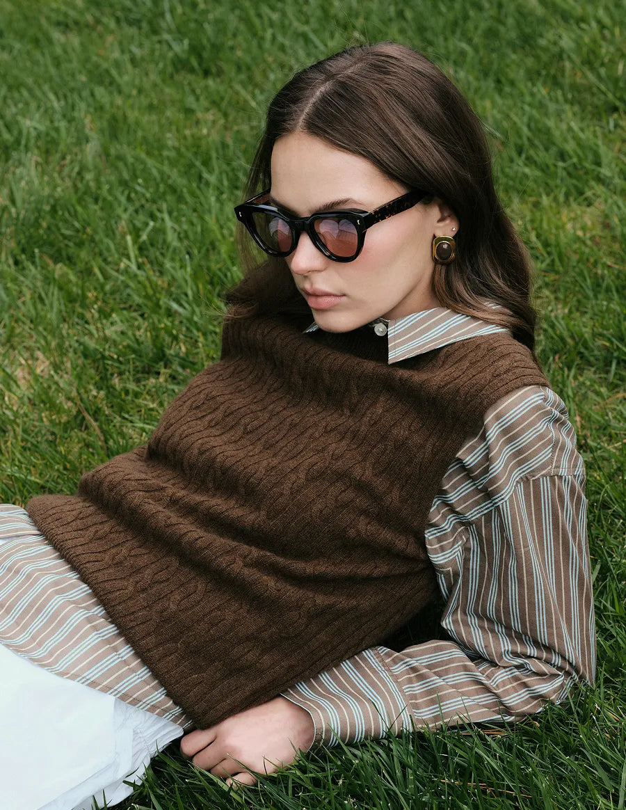 Woman wearing tortoiseshell sunglasses  with brown lenses and a brown sweater in a grassy outdoor setting