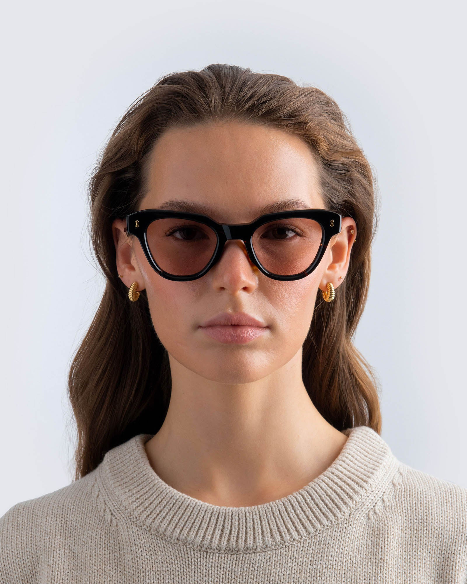 Woman wearing tortoiseshell cat-eye sunglasses with brown lenses against a light gray background