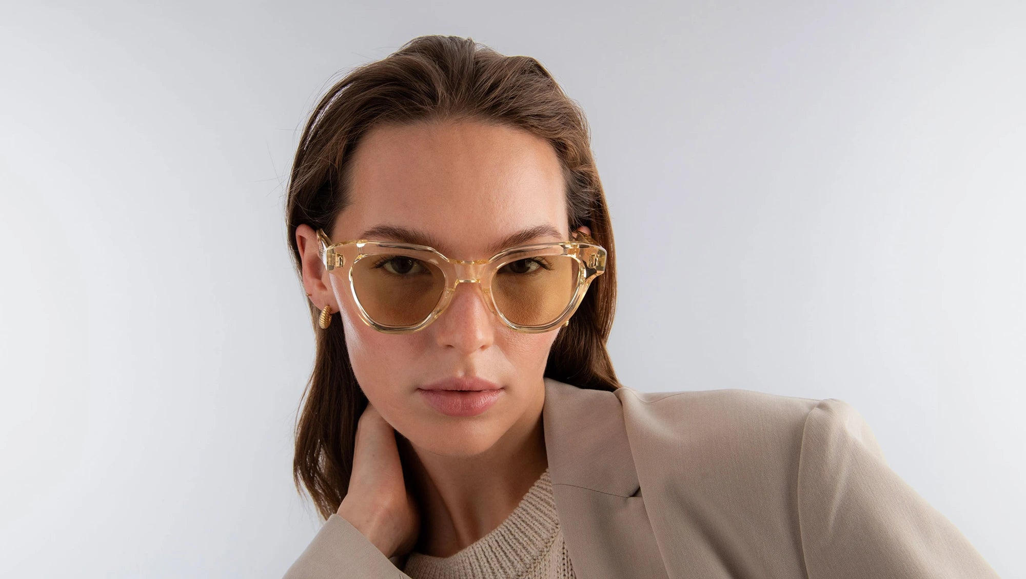 Woman wearing champagne yellow sunglasses with yellow lenses against a plain background