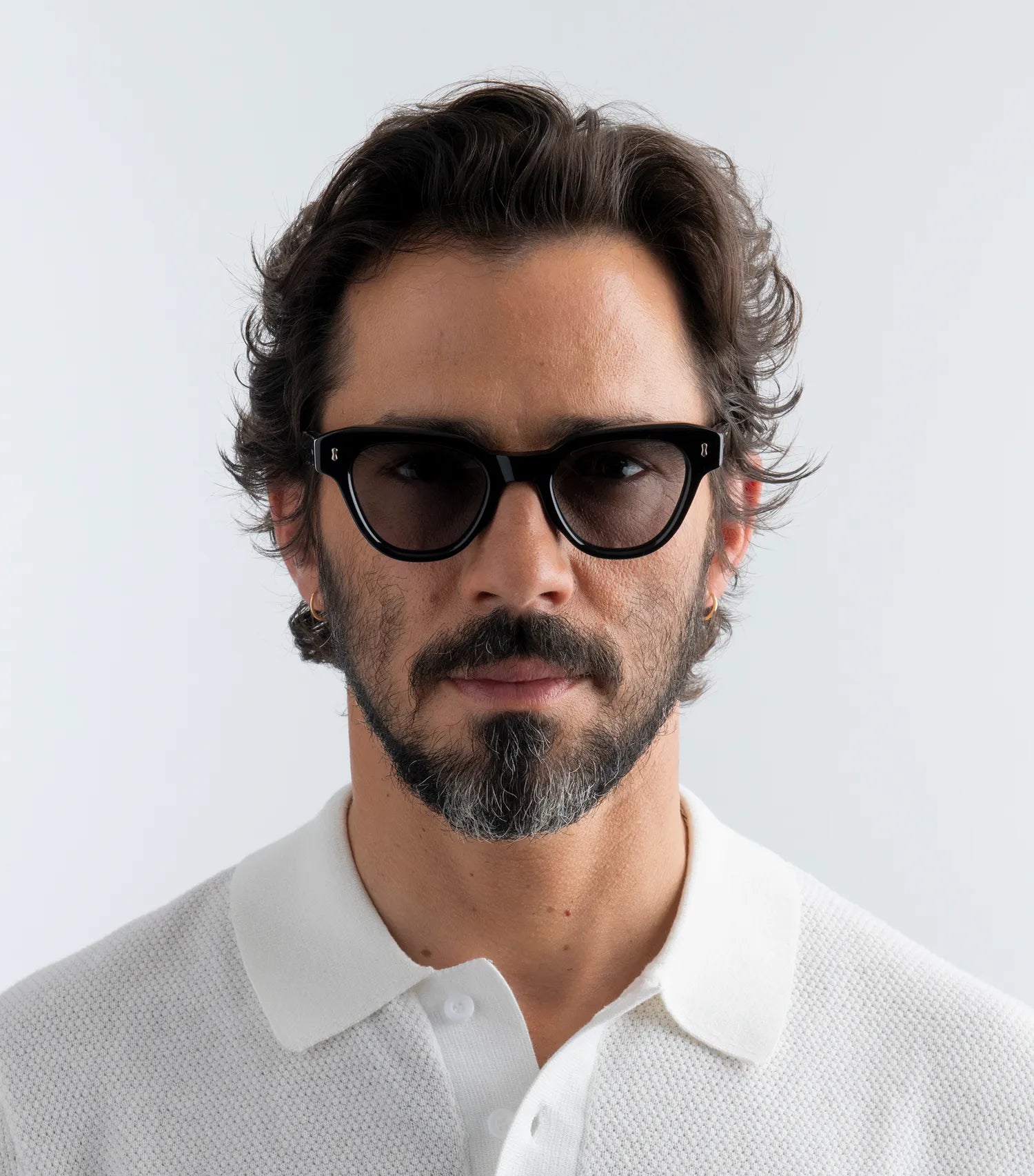 Man wearing black sunglasses with black lenses and white shirt against a light gray background