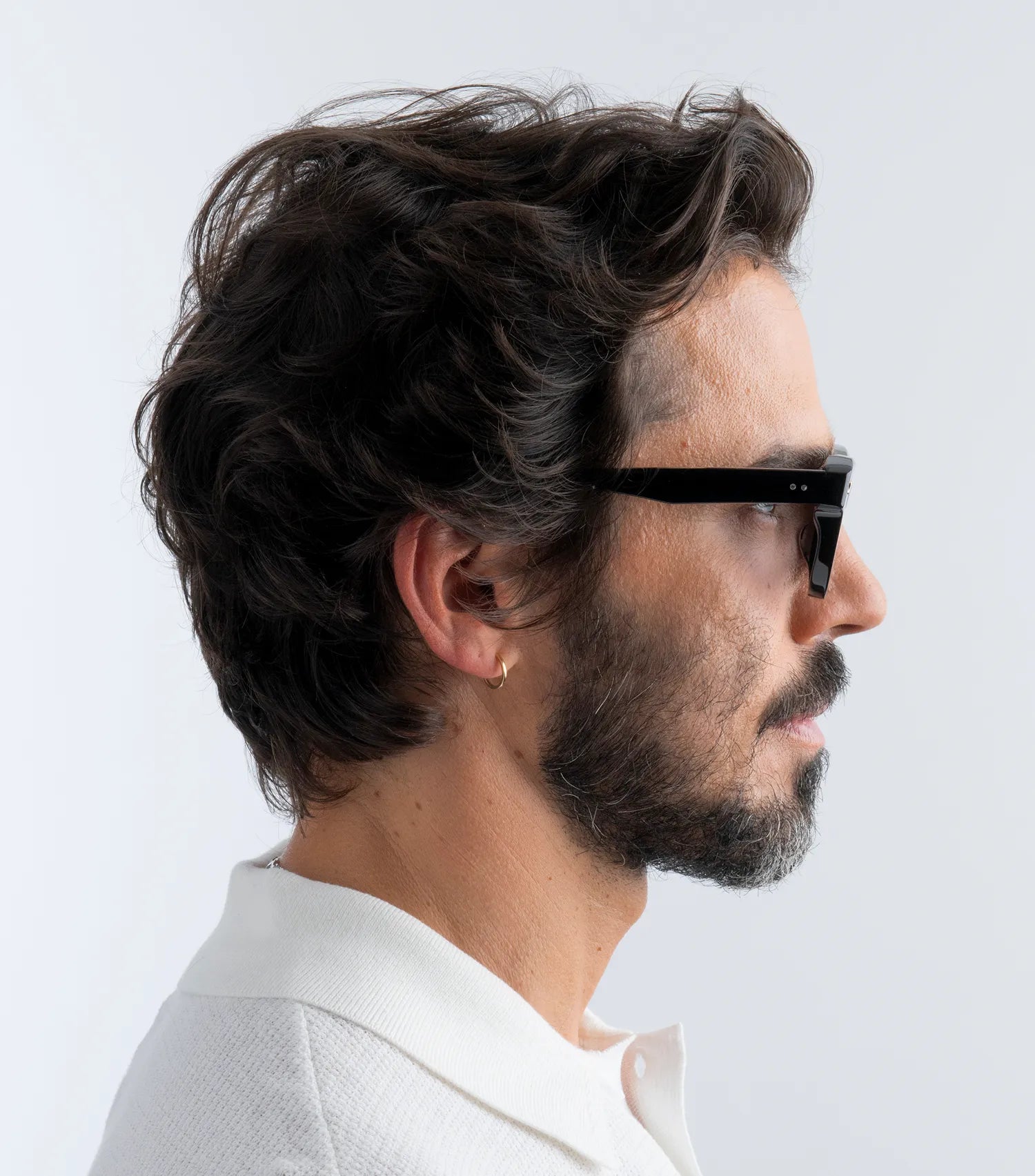Man wearing black sunglasses with black lenses and white shirt against a light gray background