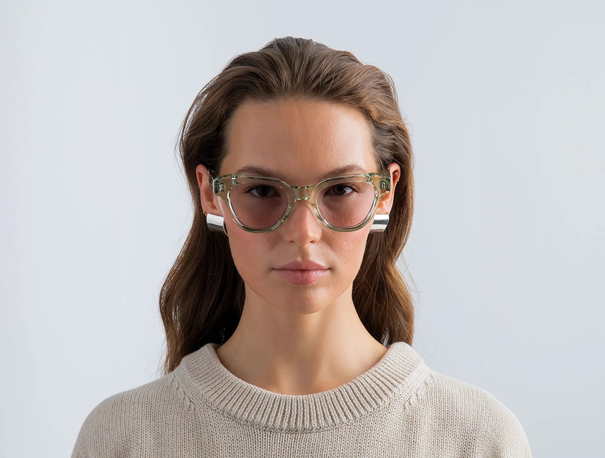 Woman wearing seafoam green glasses with lilac lenses with a plain background