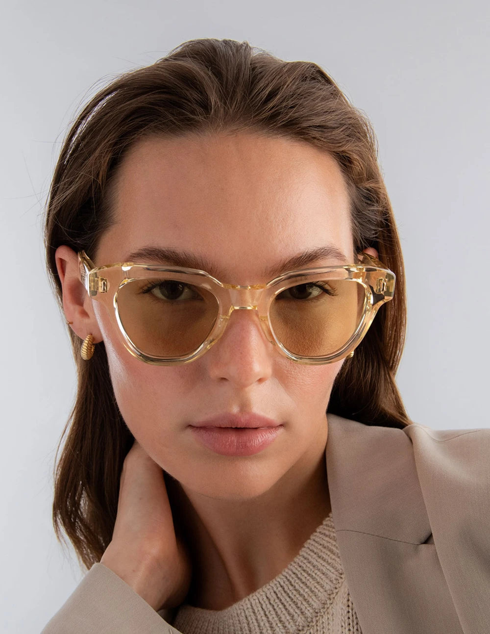 Woman wearing champagne yellow sunglasses with yellow lenses against a plain background
