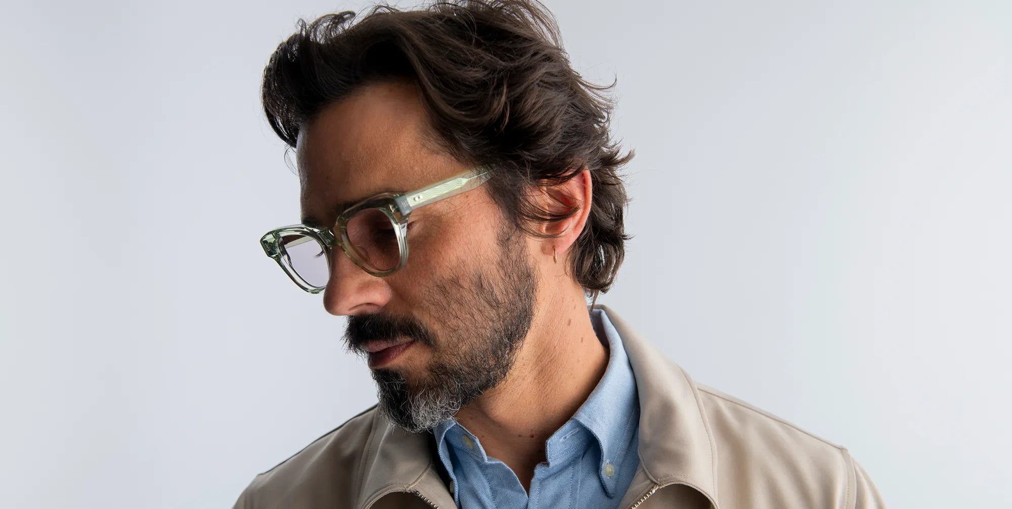 Man wearing seafoam green glasses and a beige jacket against a light gray background
