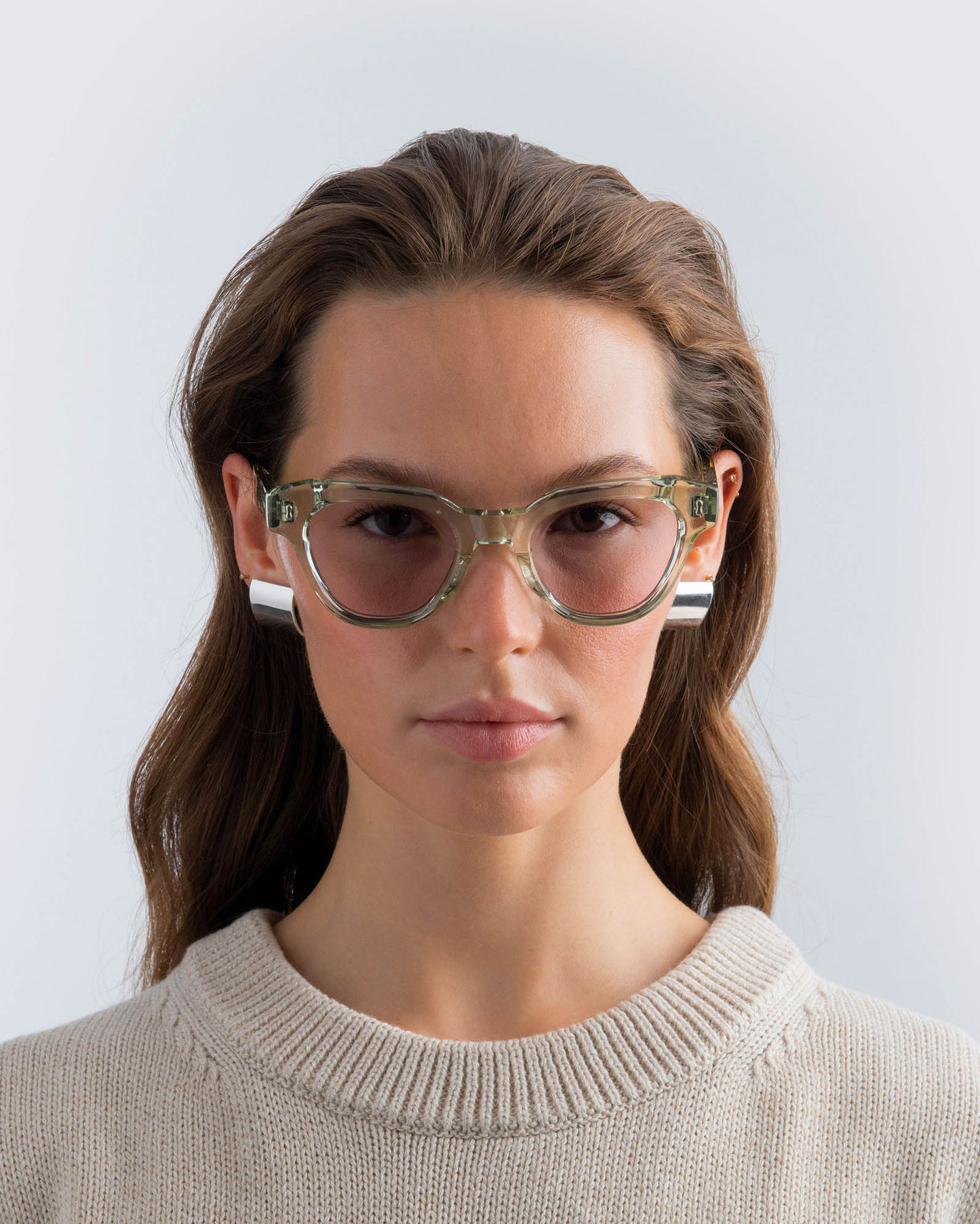 Woman wearing seafoam green sunglasses with lilac lenses against a light grey background