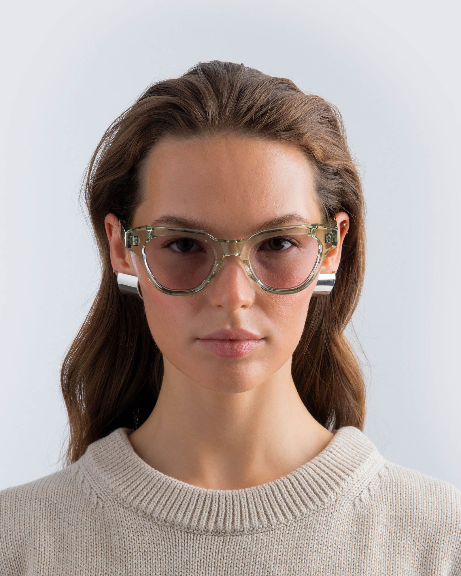 Woman wearing seafoam green sunglasses with lilac lenses against a light grey background
