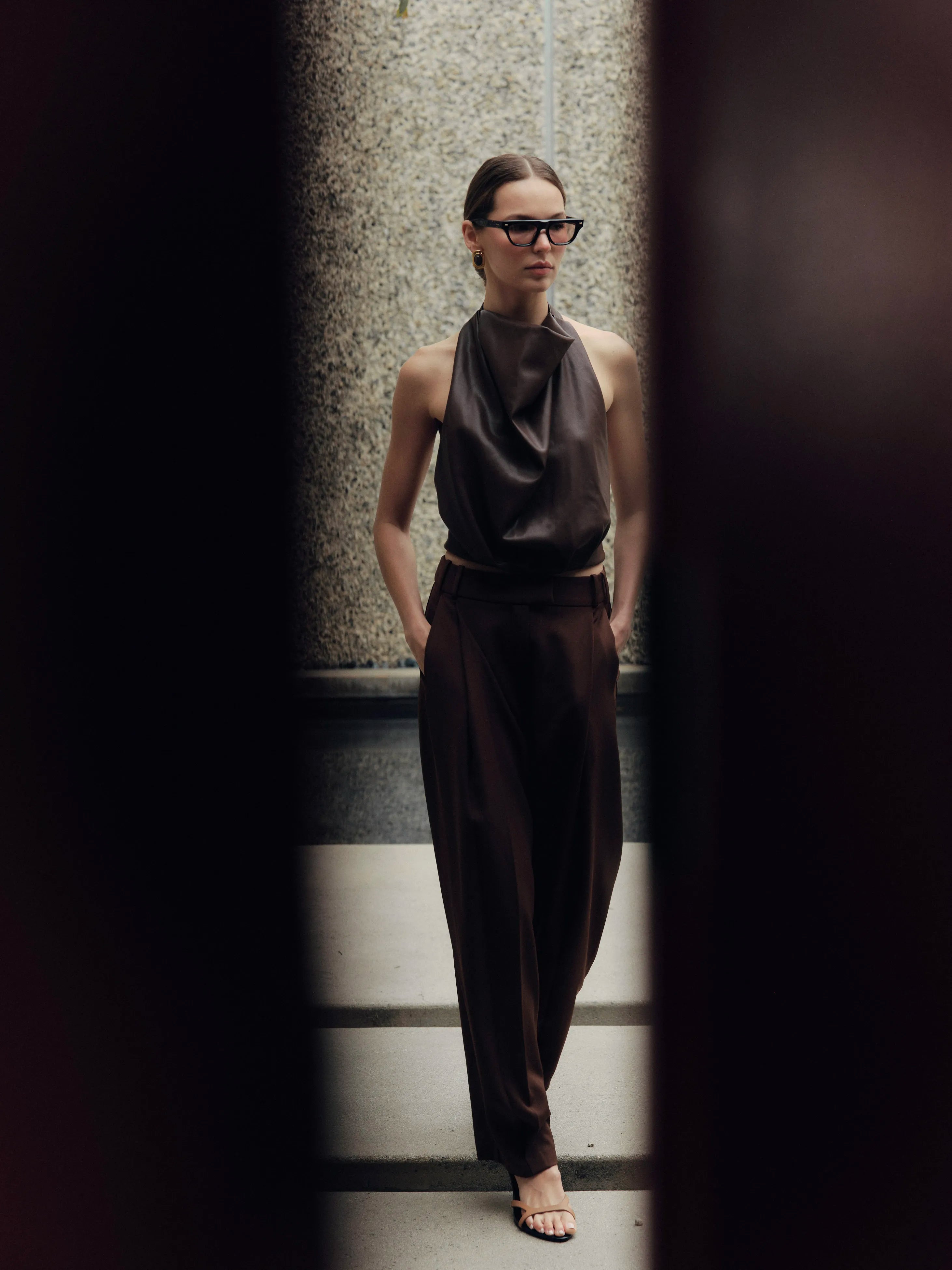 Woman wearing a dark outfit and sunglasses standing on a staircase.