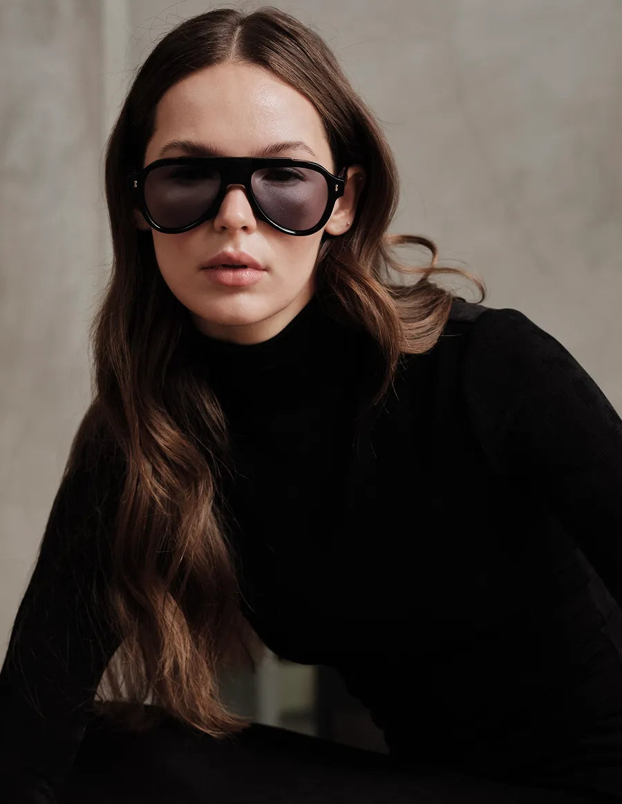 Woman wearing black sunglasses with gray lenses and a black outfit against a neutral background