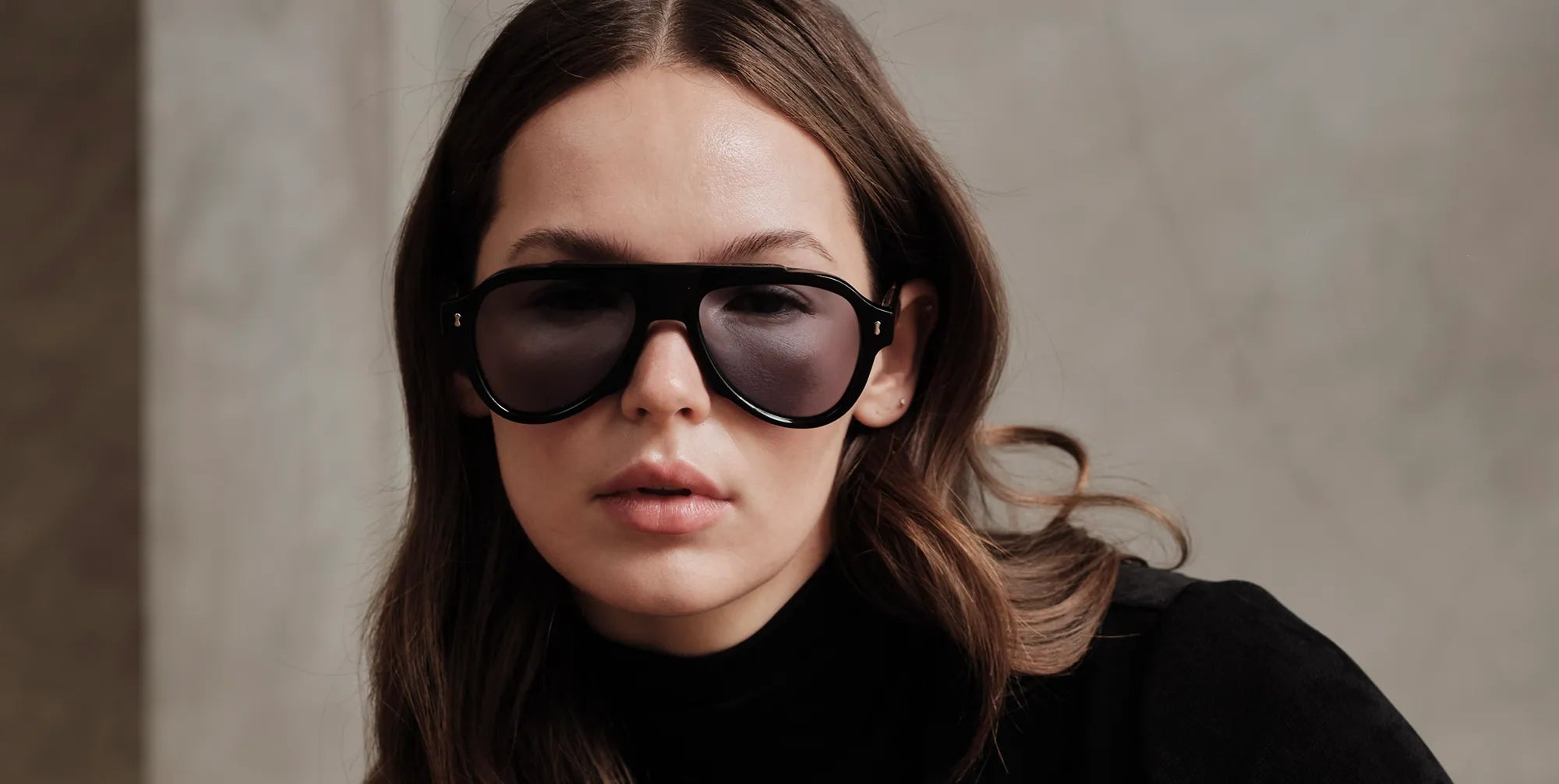 Woman wearing black sunglasses with gray lenses and a black outfit against a neutral background