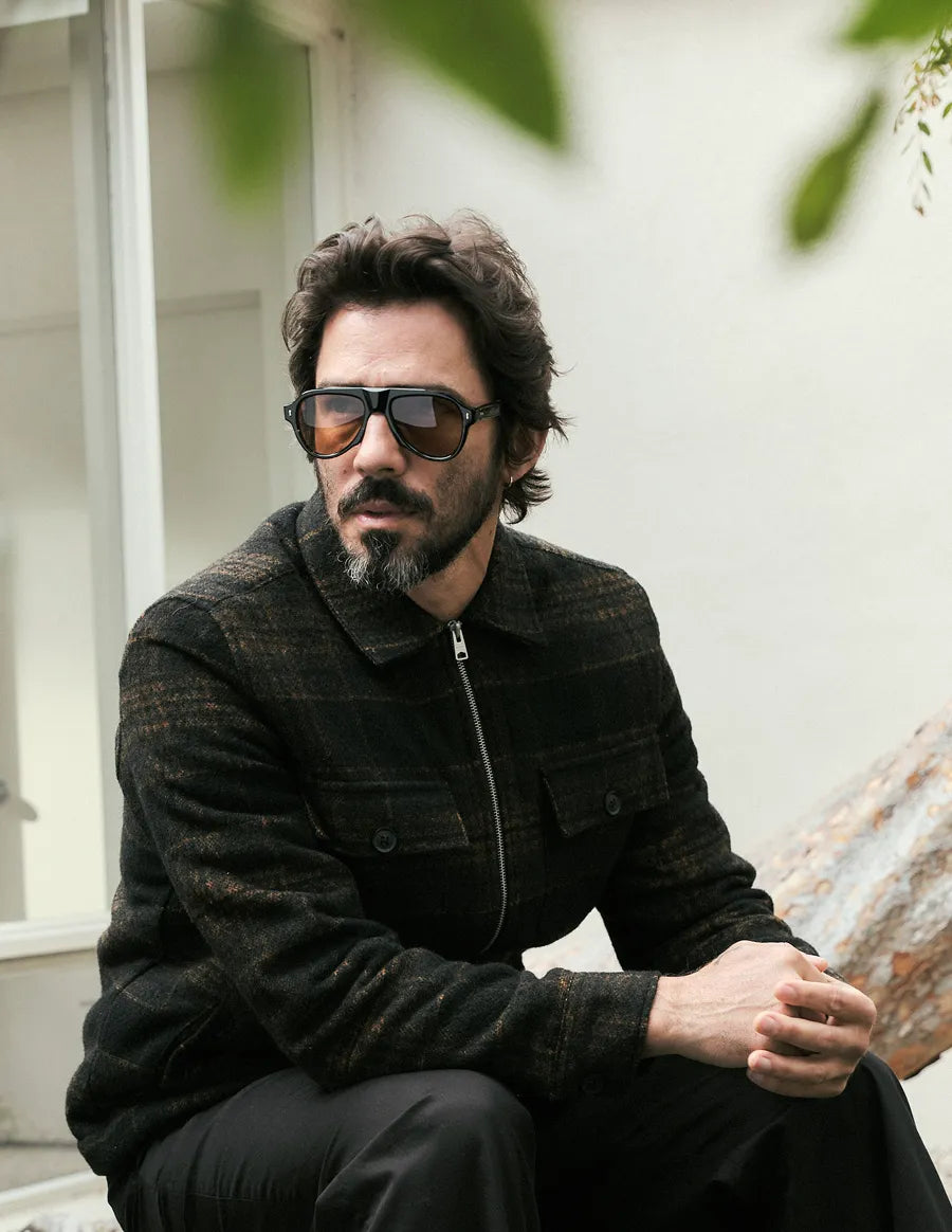 Man wearing tortoiseshell sunglasses with amber lenses and a dark jacket sitting outdoors