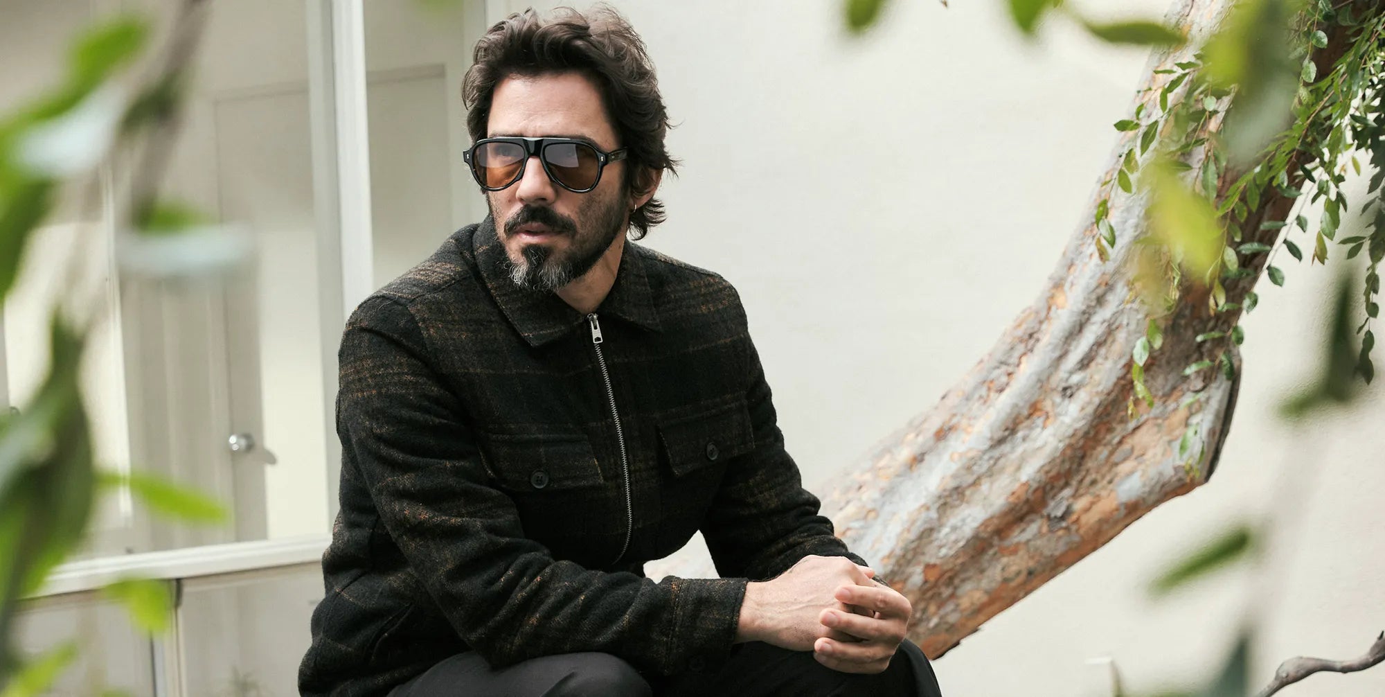 Man wearing tortoiseshell sunglasses with amber lenses and a dark jacket sitting outdoors