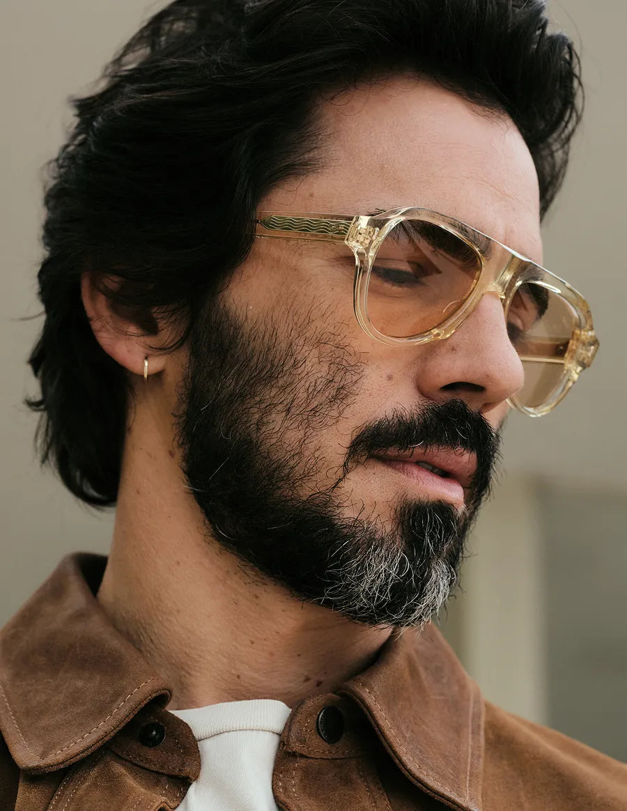 Man wearing champagne sunglasses and a brown jacket with a neutral background